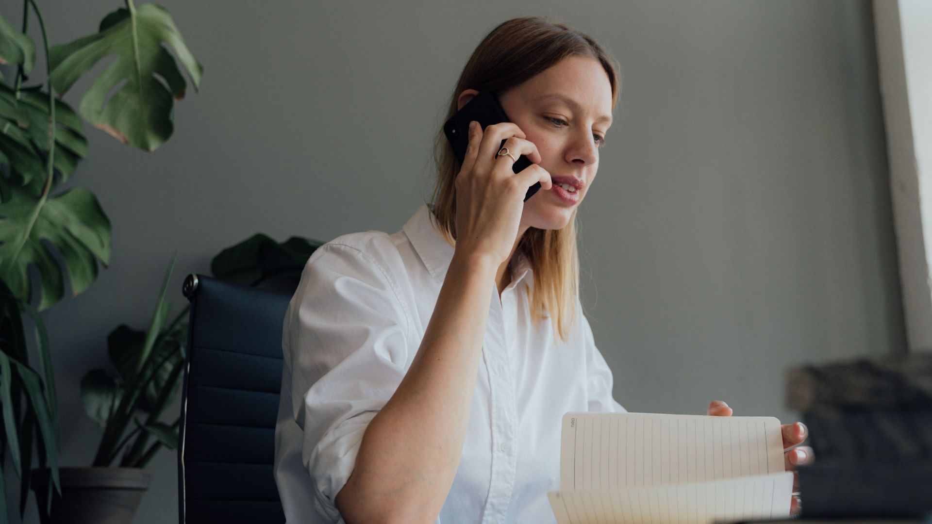 Woman on a phone call while reviewing documents at her desk indoors.