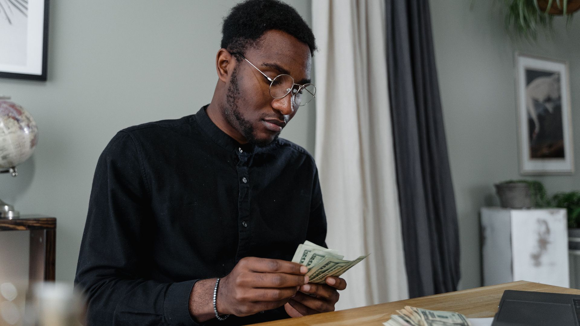A focused man in glasses counting cash at a desk, indicating financial management.