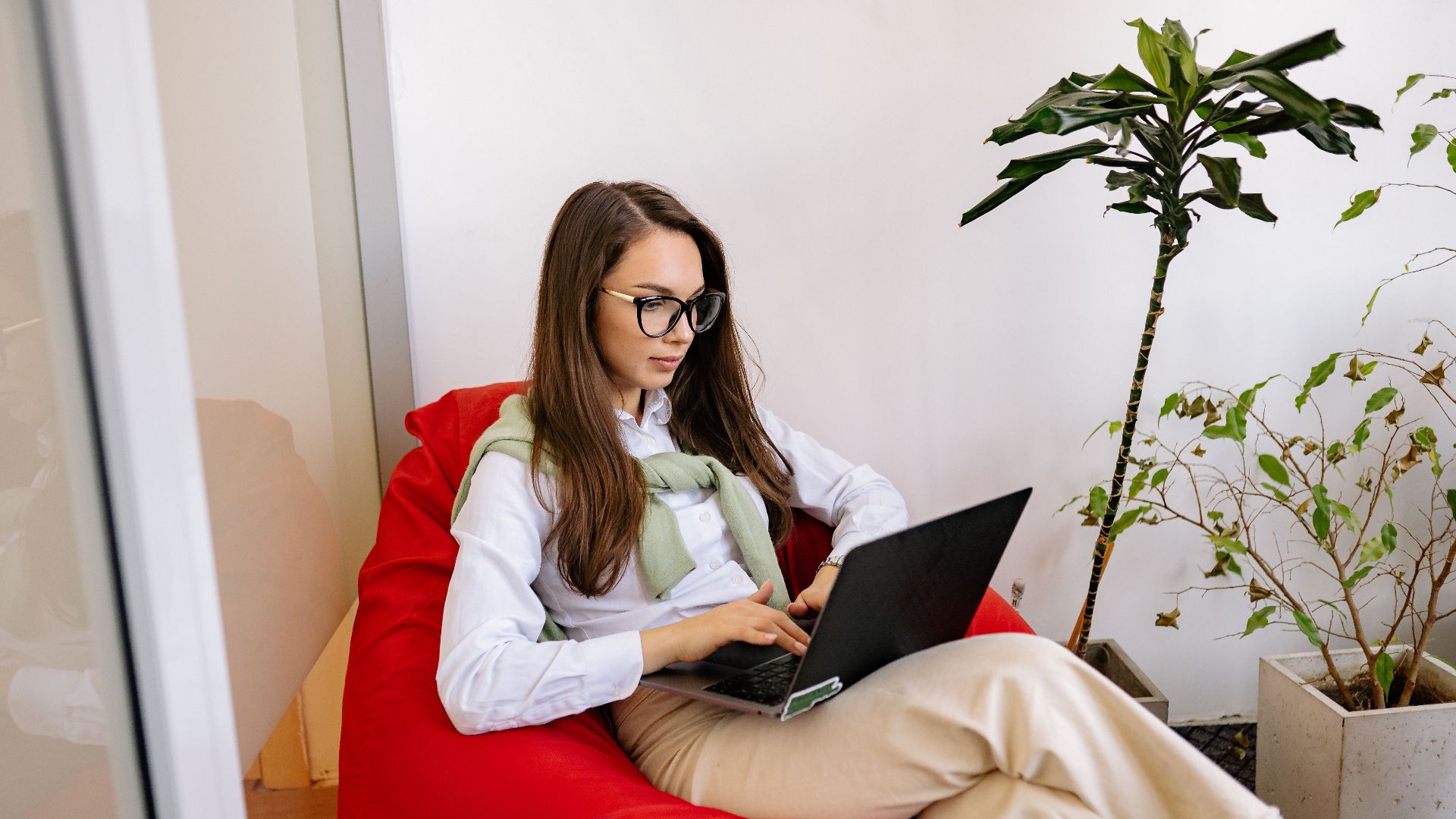 Woman working on laptop while relaxing in a bean bag in modern indoor setting.