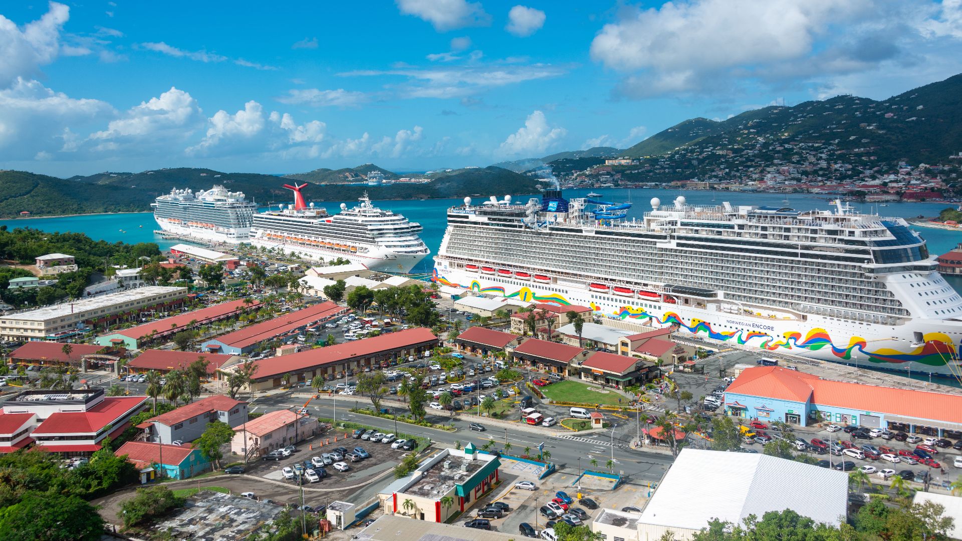 Stunning aerial view of luxurious cruise ships docked in a scenic harbor with hills and clear skies.