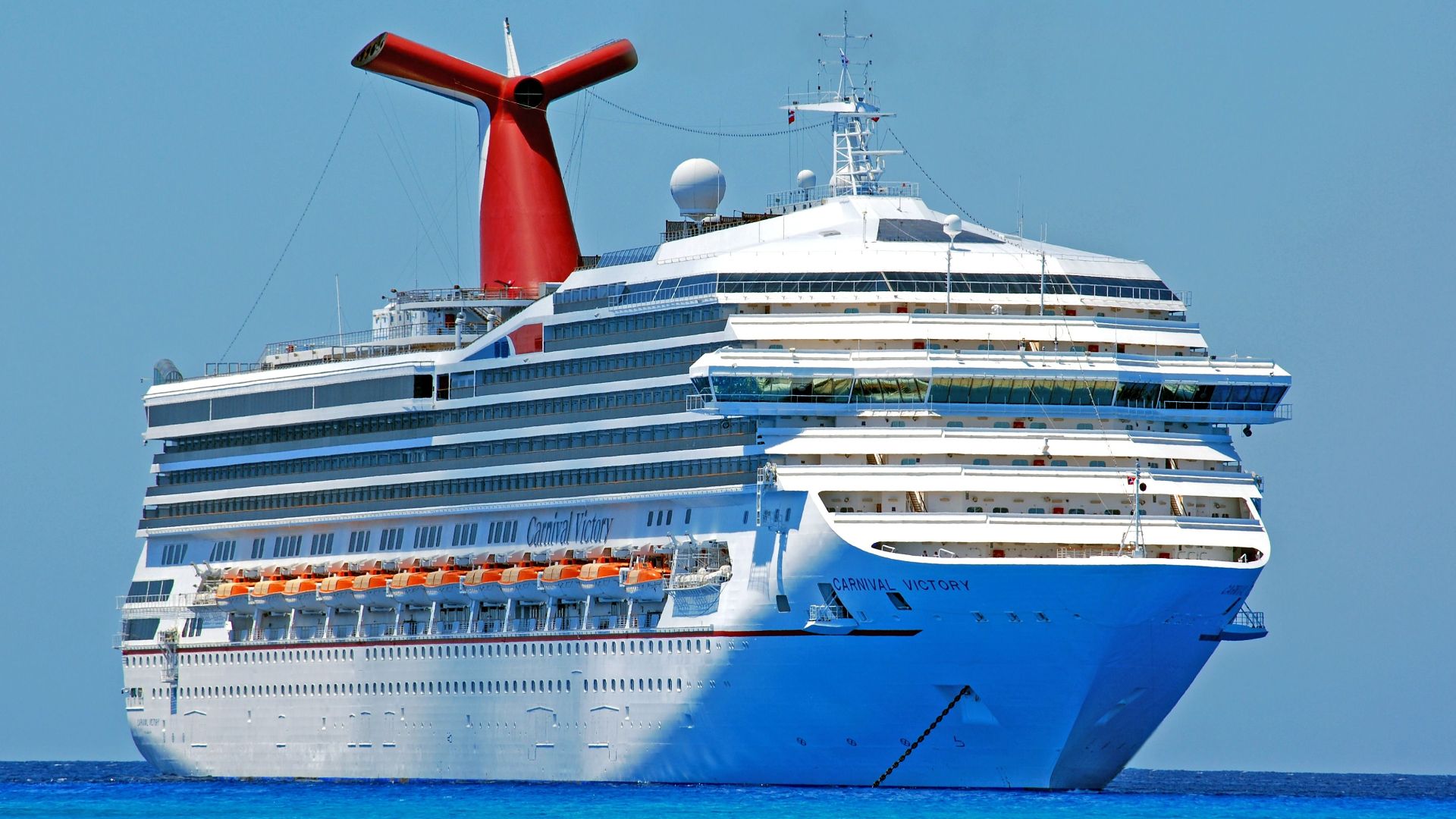 A large cruise ship gliding through clear blue ocean waters on a sunny day.