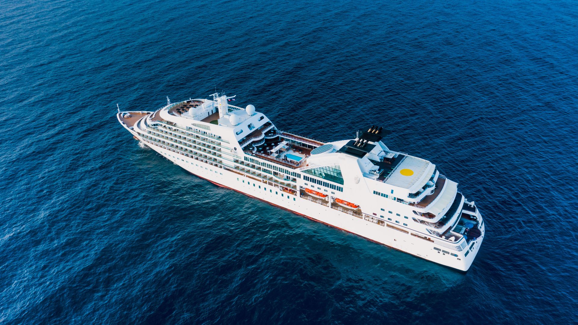 Drone view of luxury modern cruise ship floating on rippling blue water of ocean in sunny day