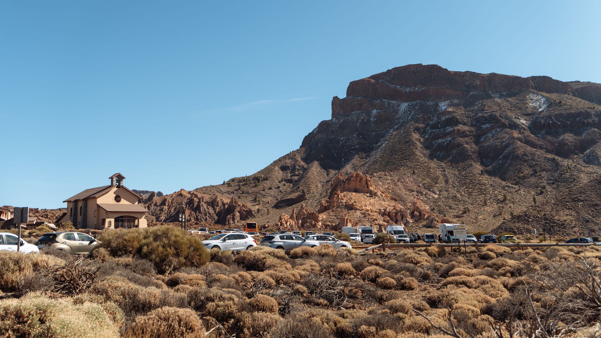 A scenic view of a chapel and cars against rocky mountains in Tenerife.