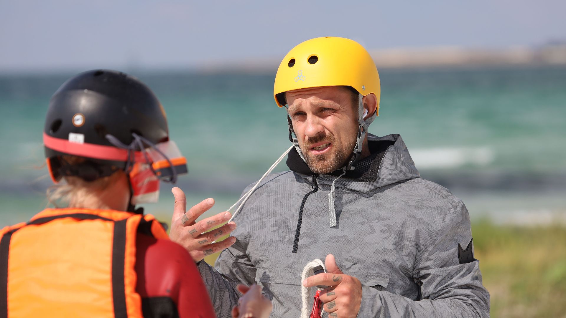 Two adults discussing safety and strategy with helmets by the sea.