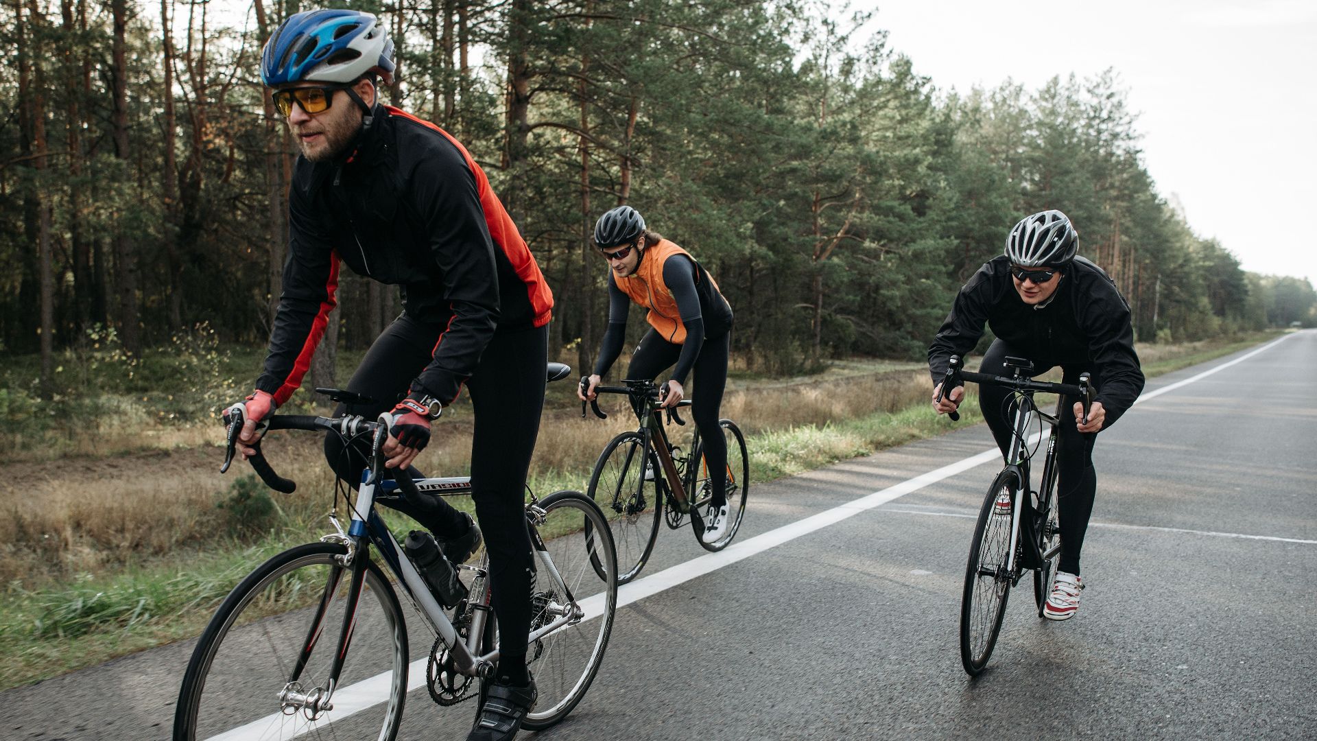 Three cyclists in activewear enjoy a ride along a scenic forest road at daytime.