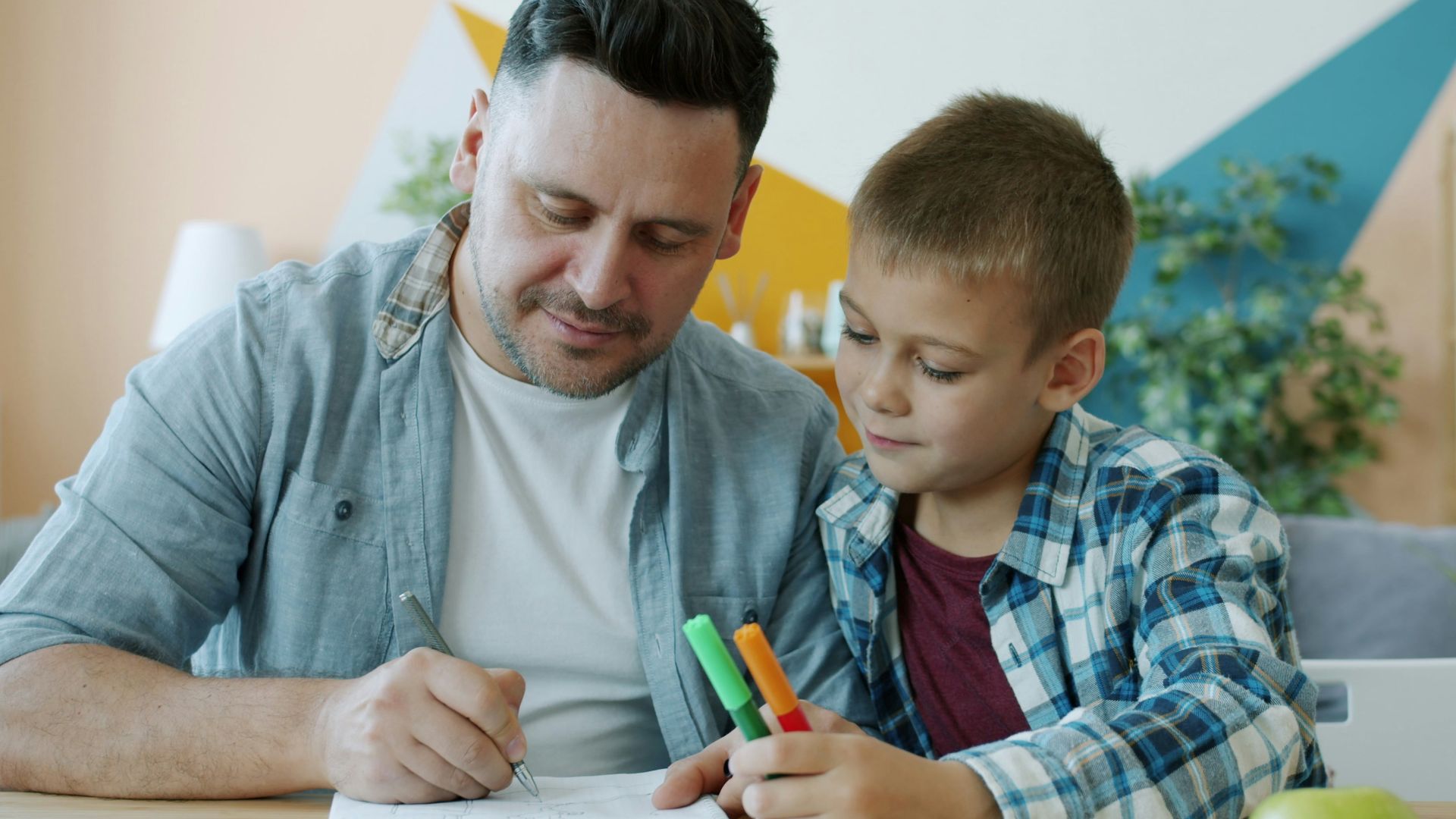 Father and son drawing together at a table.