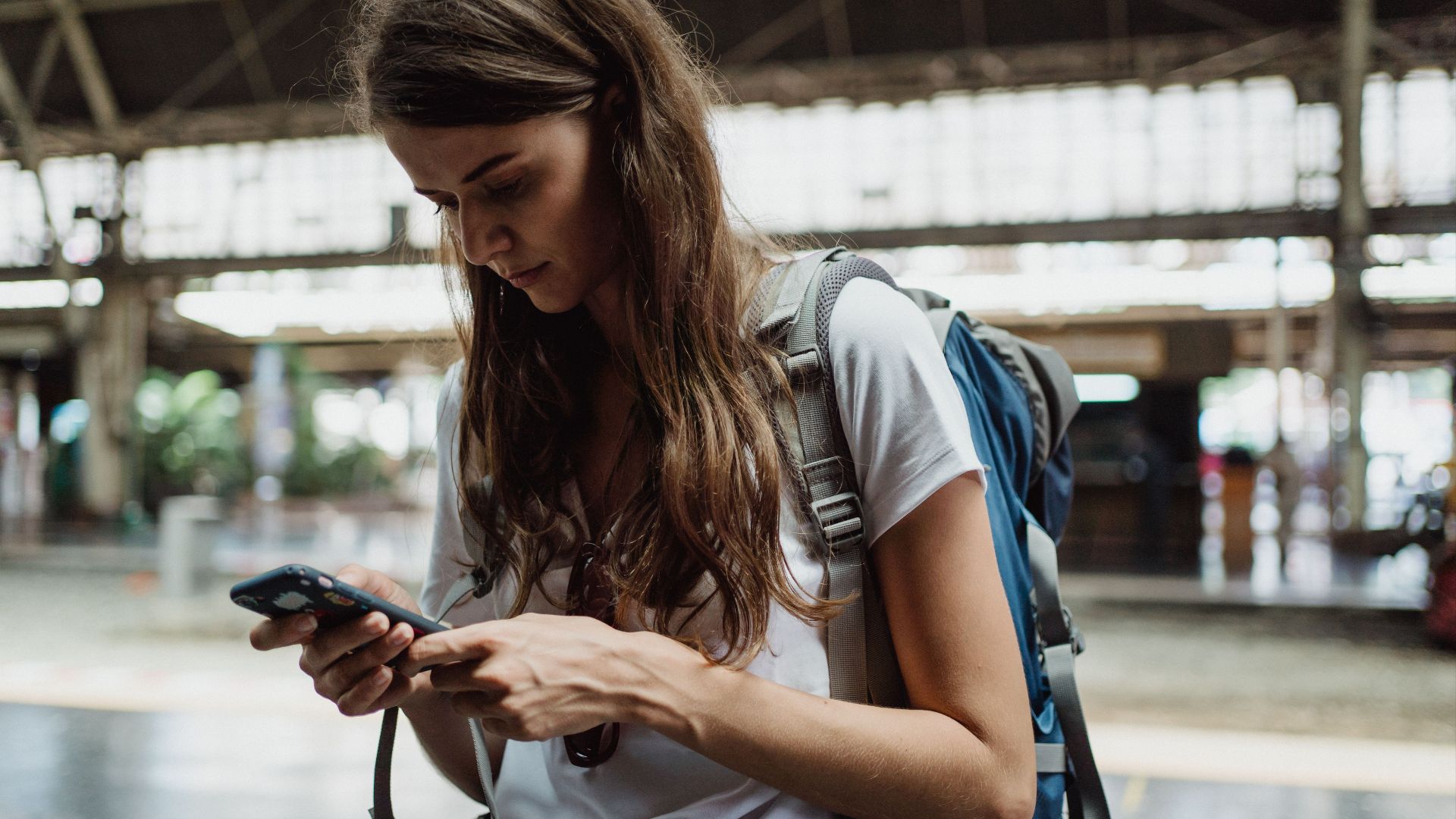 A young woman checks her smartphone while traveling at a train station.