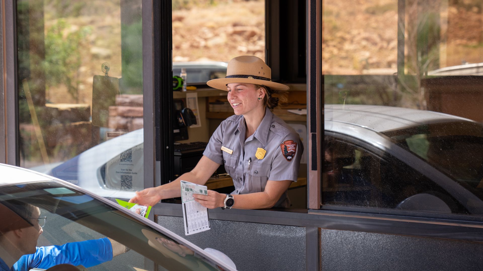 A smiling fee ranger hands a visitor in their car information sheets from the fee booth.
National Park Service rangers manage entrance stations in Zion National Park.
Memorial Day Weekend 2022 fee stations and Zion Canyon Visitor Center near Springdale, U