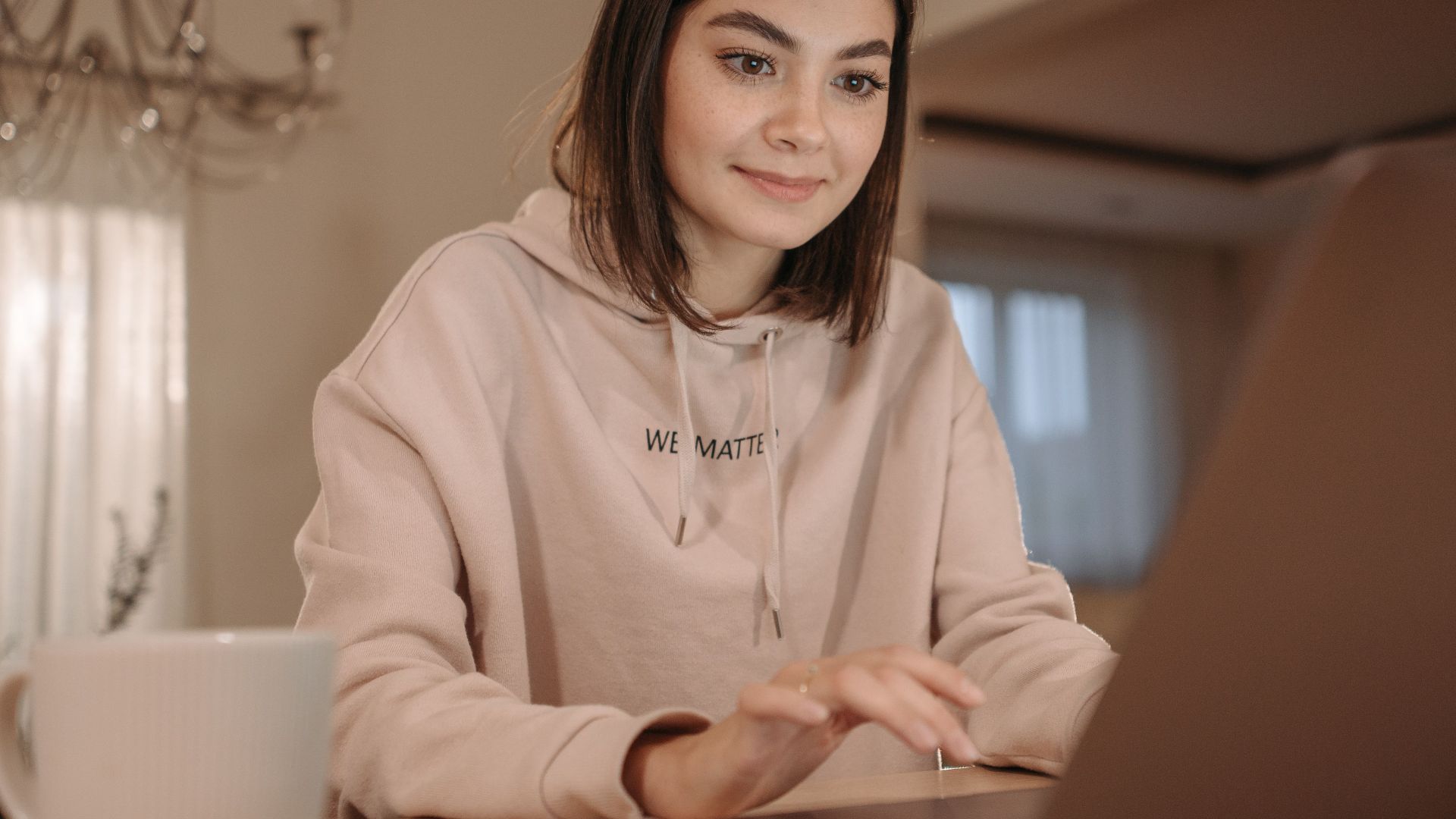A young woman in a cozy setting using a laptop with a cup of coffee nearby.