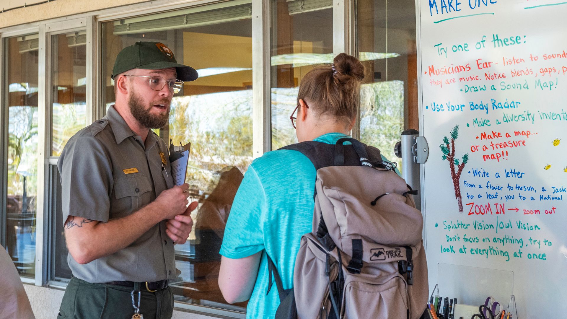 NPS / Emily Hassell

Alt text: A park ranger talks with a visitor outside of the Oasis of Mara Visitor Center in front of a table of drawing supplies.