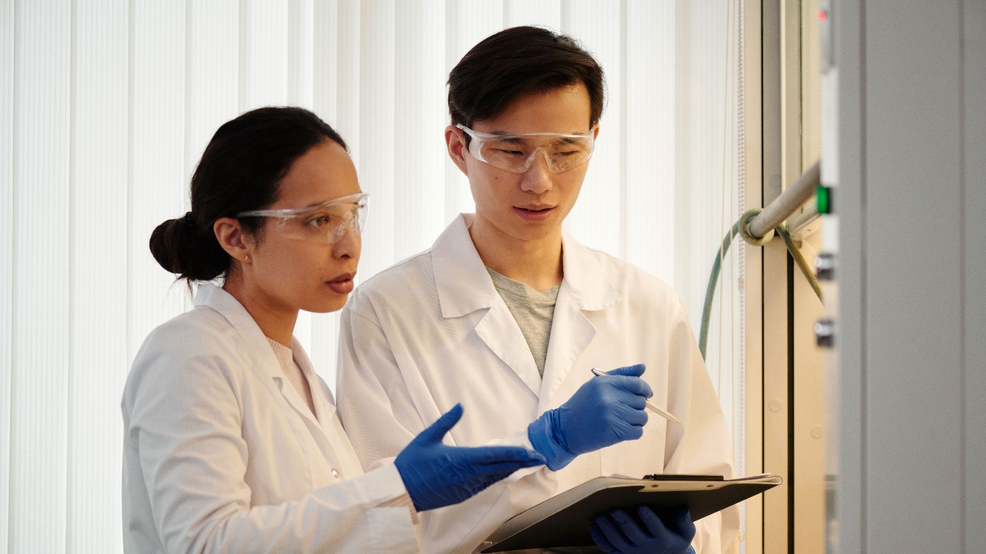 Researchers discussing data in a laboratory setting, wearing safety gear and blue gloves.