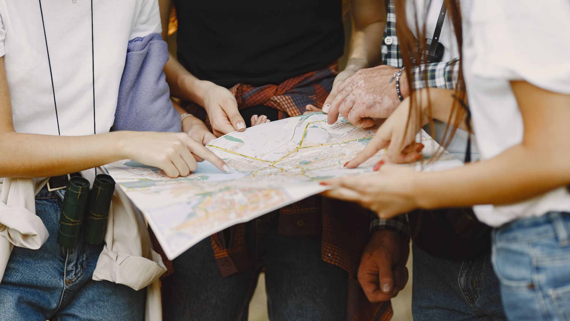 Young adults examining map on outdoor exploration, daytime travel planning.