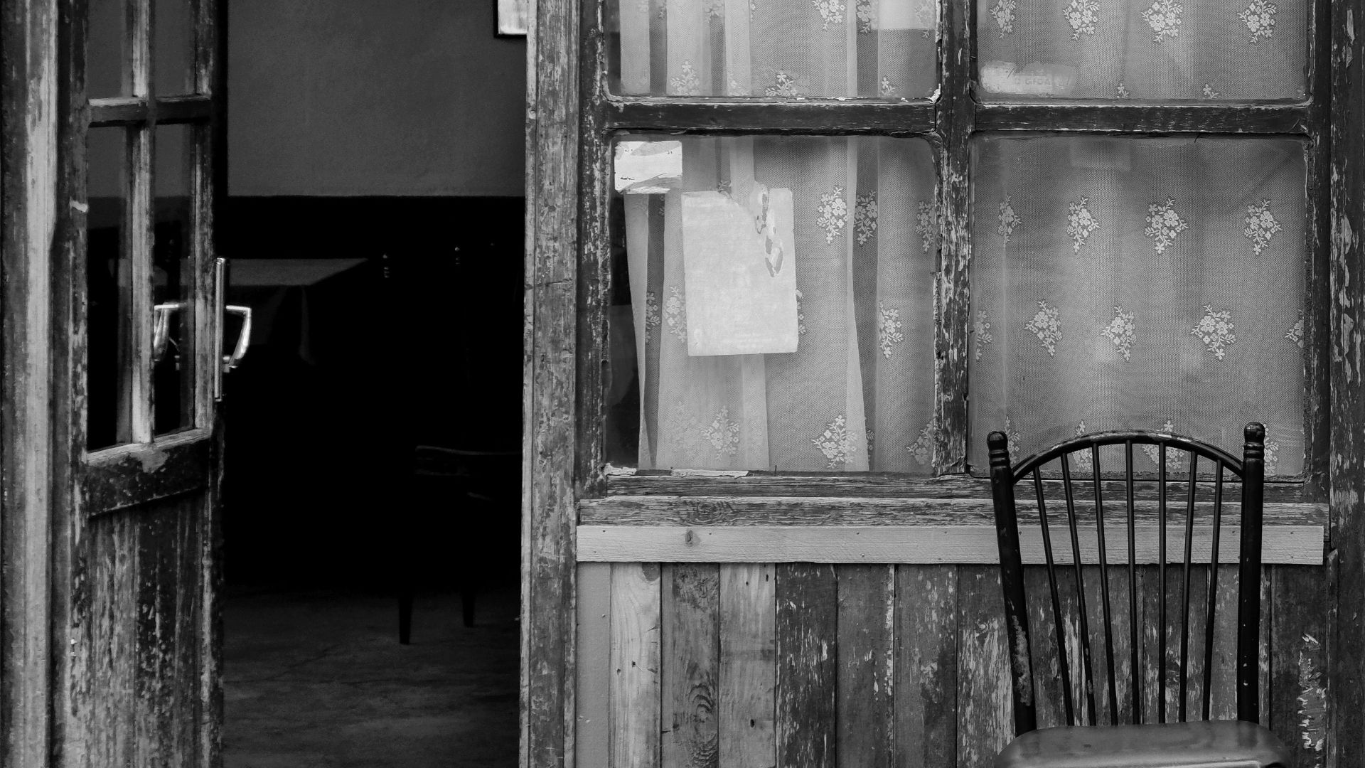 Black and white photo of an old wooden door with a chair, depicting vintage style.