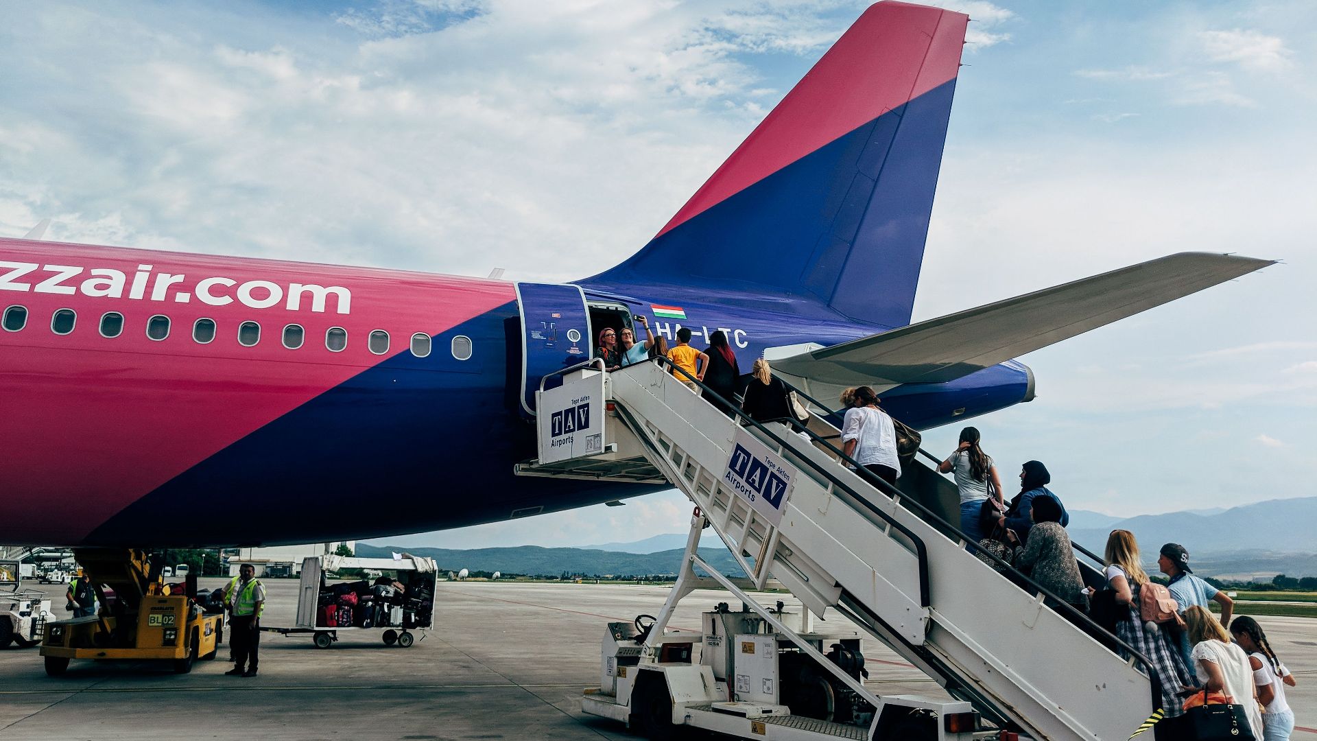 Travelers boarding a WizzAir Airbus A320 jet on a clear day at the airport.