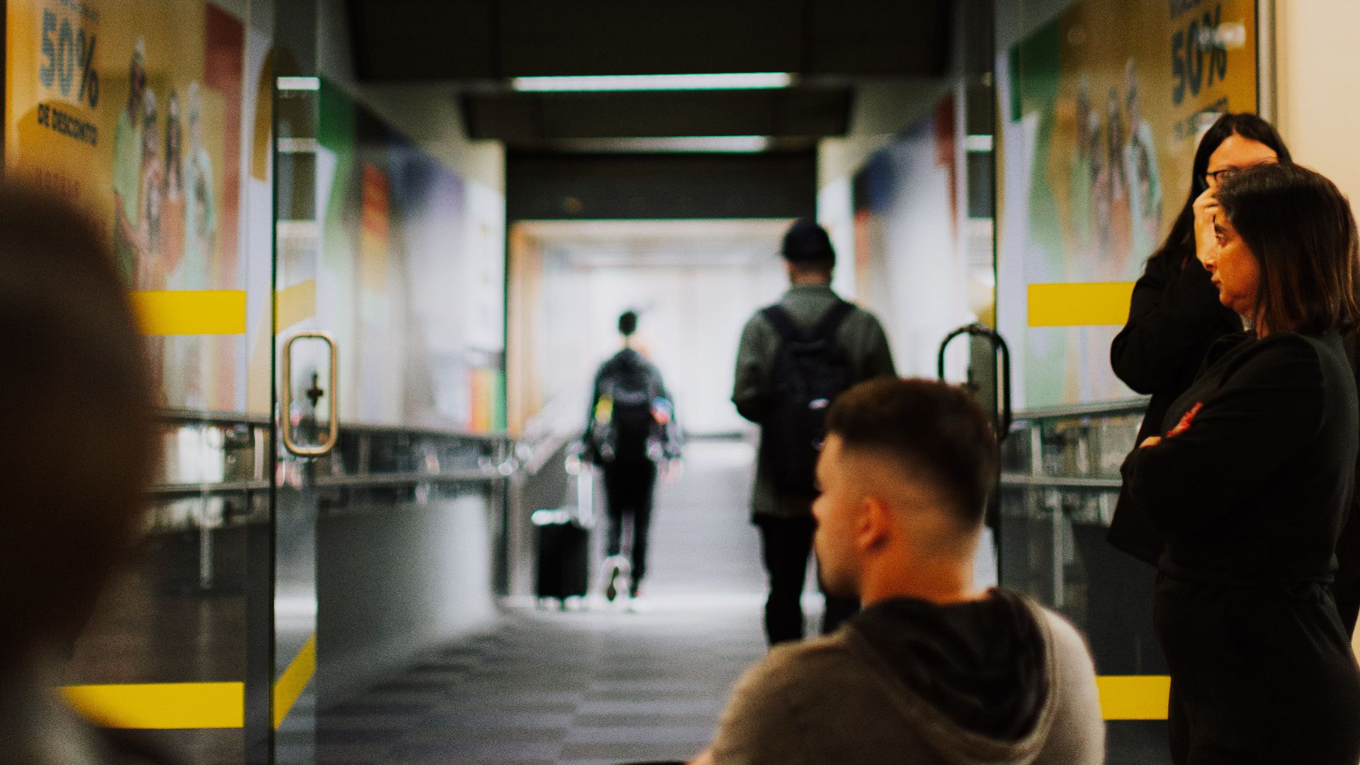 Travelers waiting at a bustling airport gate with a focus on the entrance and sign.