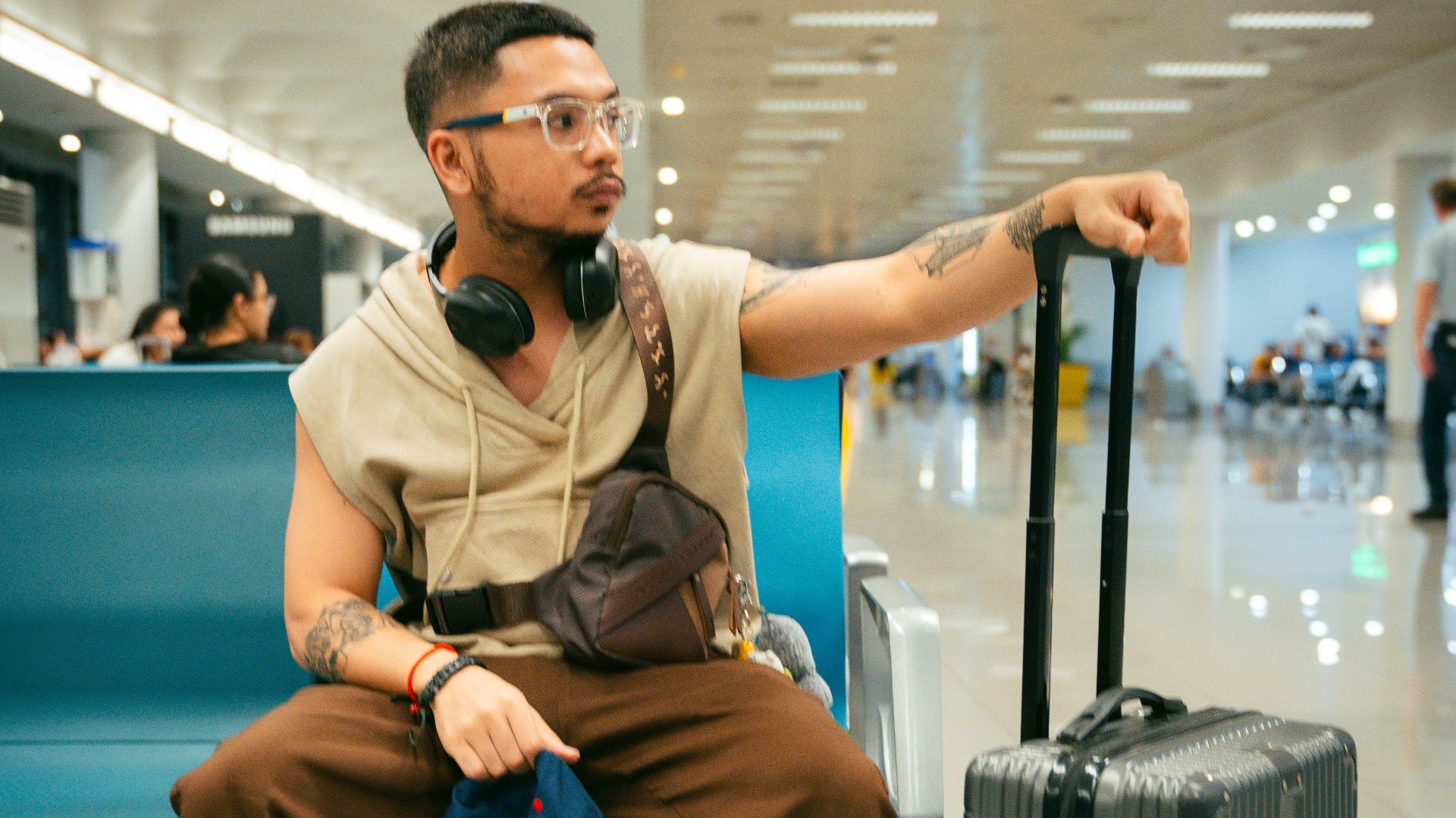 Stylish young man with suitcase seated in airport terminal, looking alert and prepared for travel.