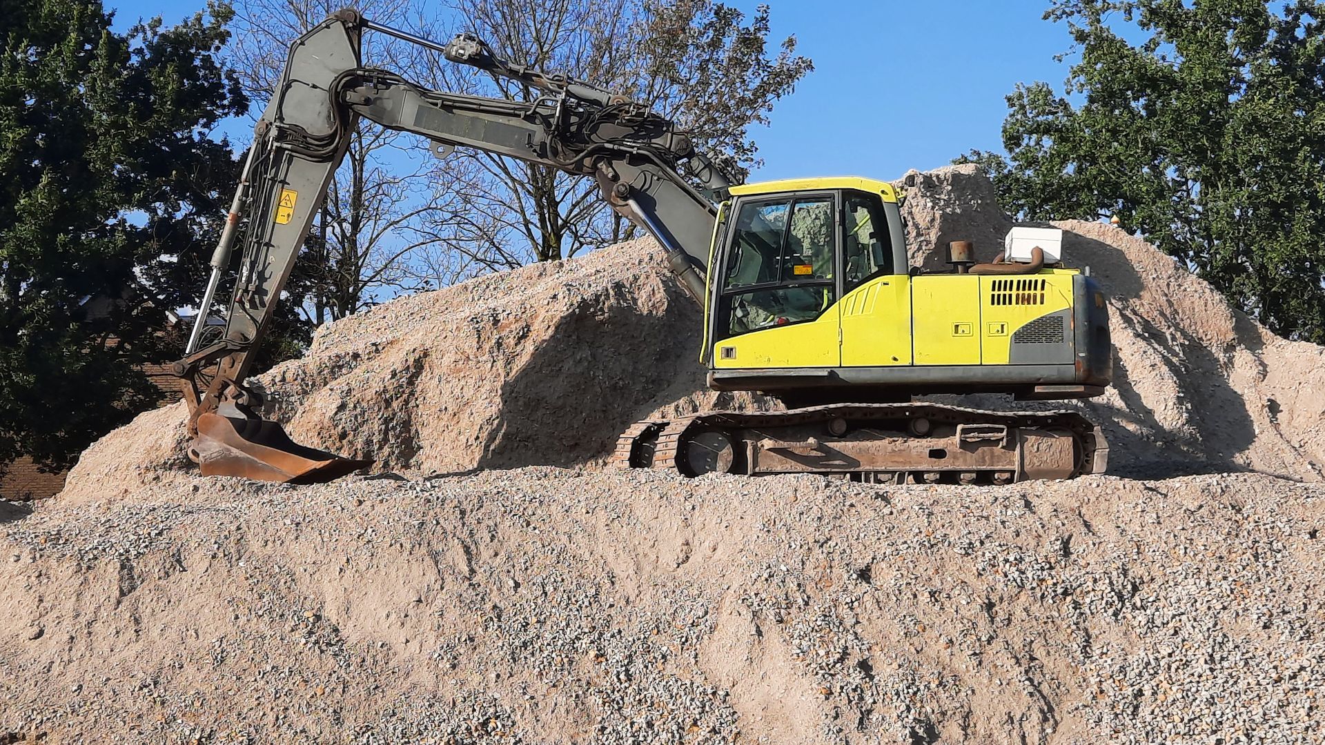 A yellow excavator working on a gravel mound at a construction site.