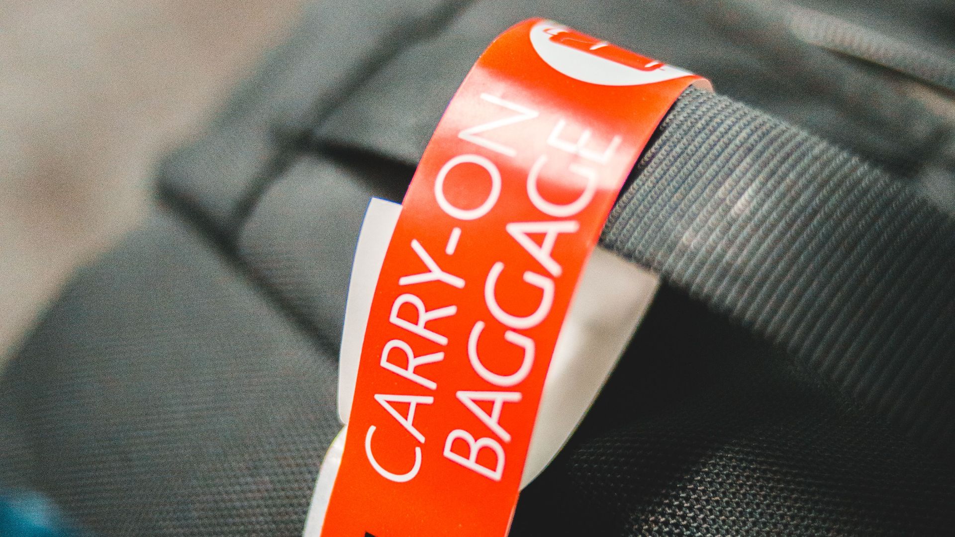 Detailed image of a carry-on baggage tag attached to a gray travel bag, indicating air travel.