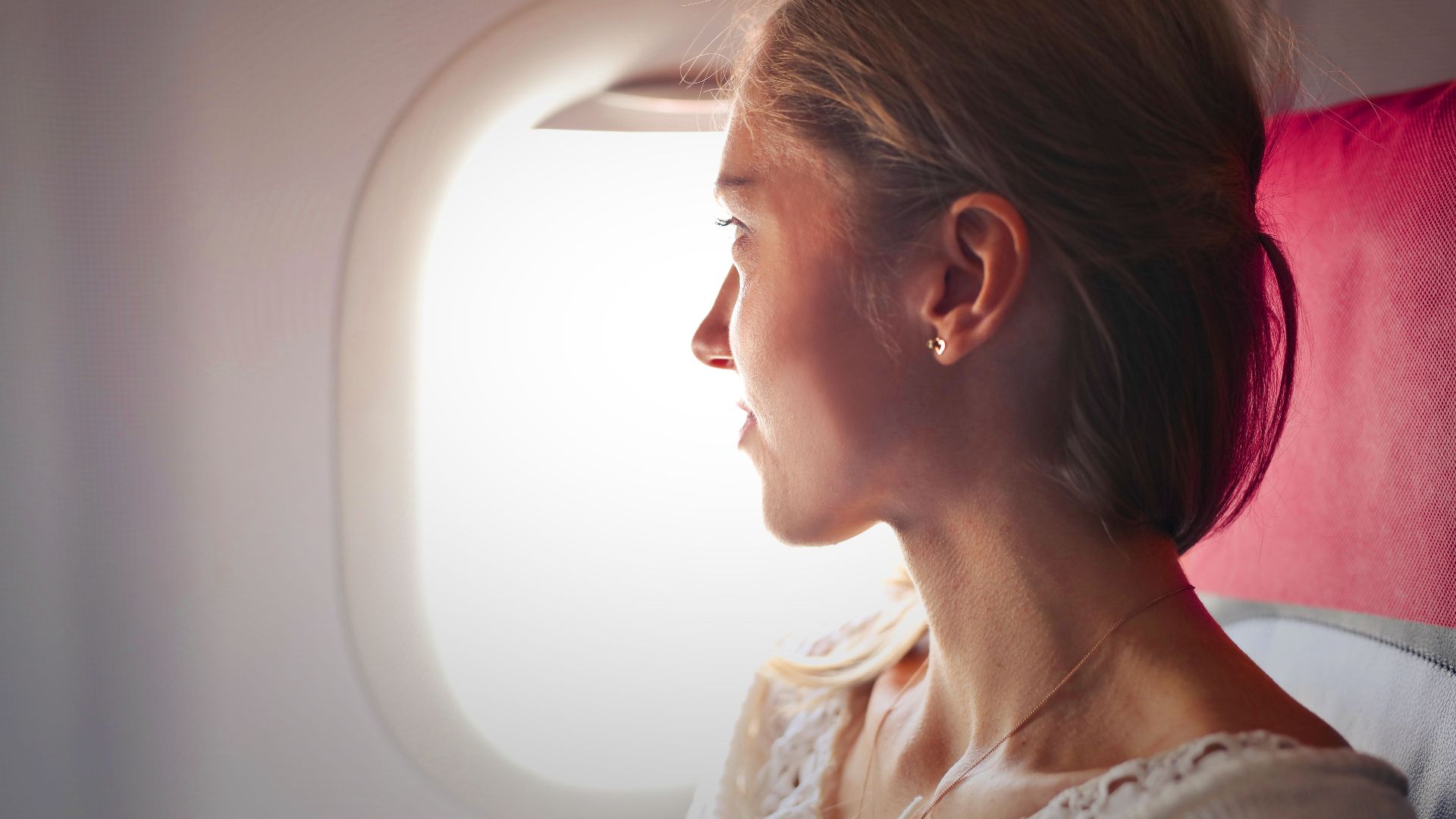 A woman gazes thoughtfully out the window of an airplane during her journey.