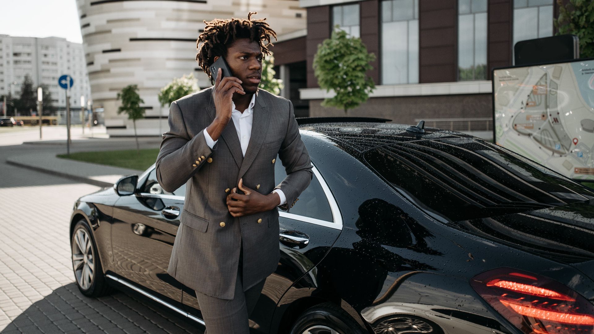 Confident businessman making a phone call while standing beside a luxury black car in an urban setting.