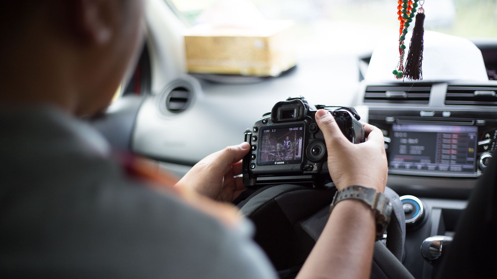 Photographer holding DSLR camera inside car, checking images and settings.