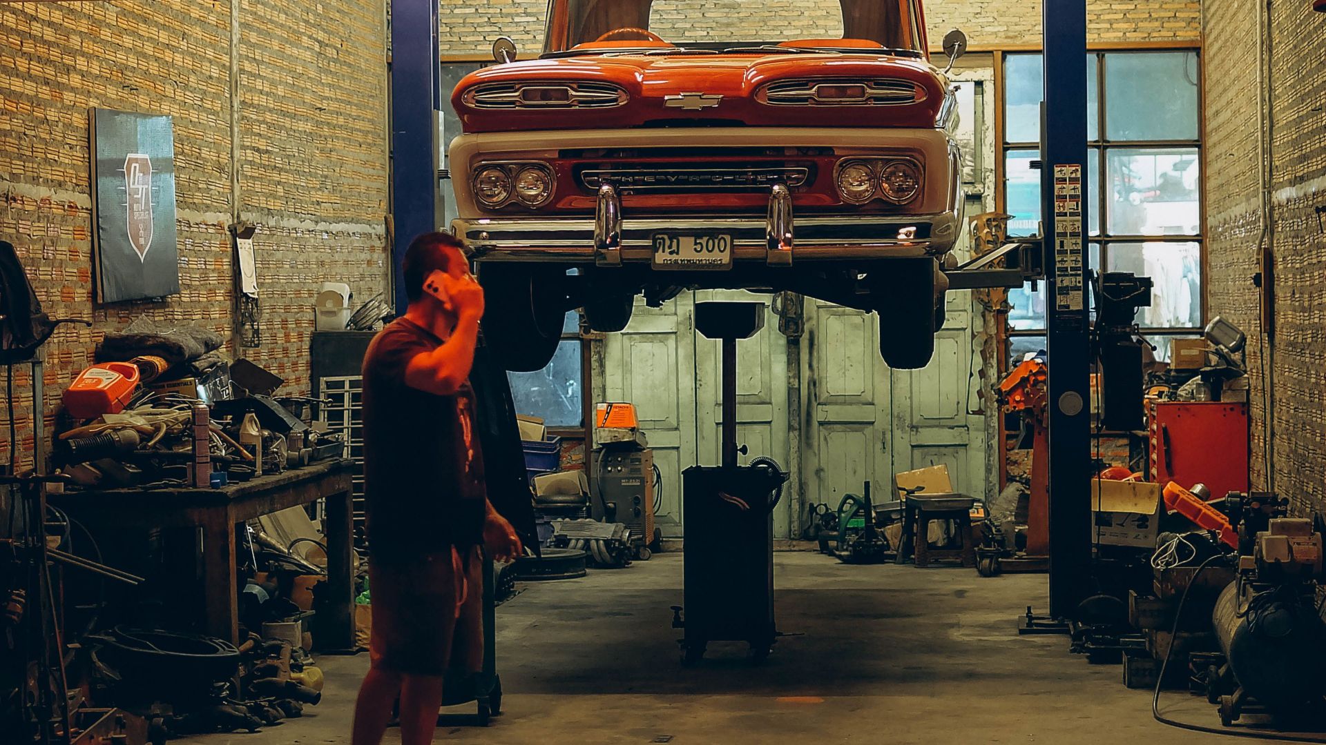 A red vintage truck is lifted in a Bangkok garage. Industrial setting with nostalgic automotive elements.