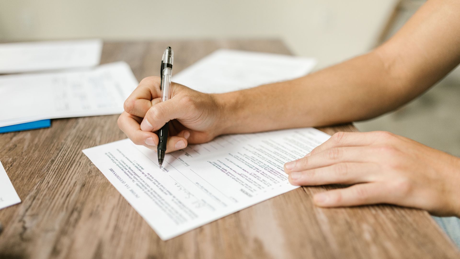 Hand filling out paperwork with a pen, showcasing focus on document completion.