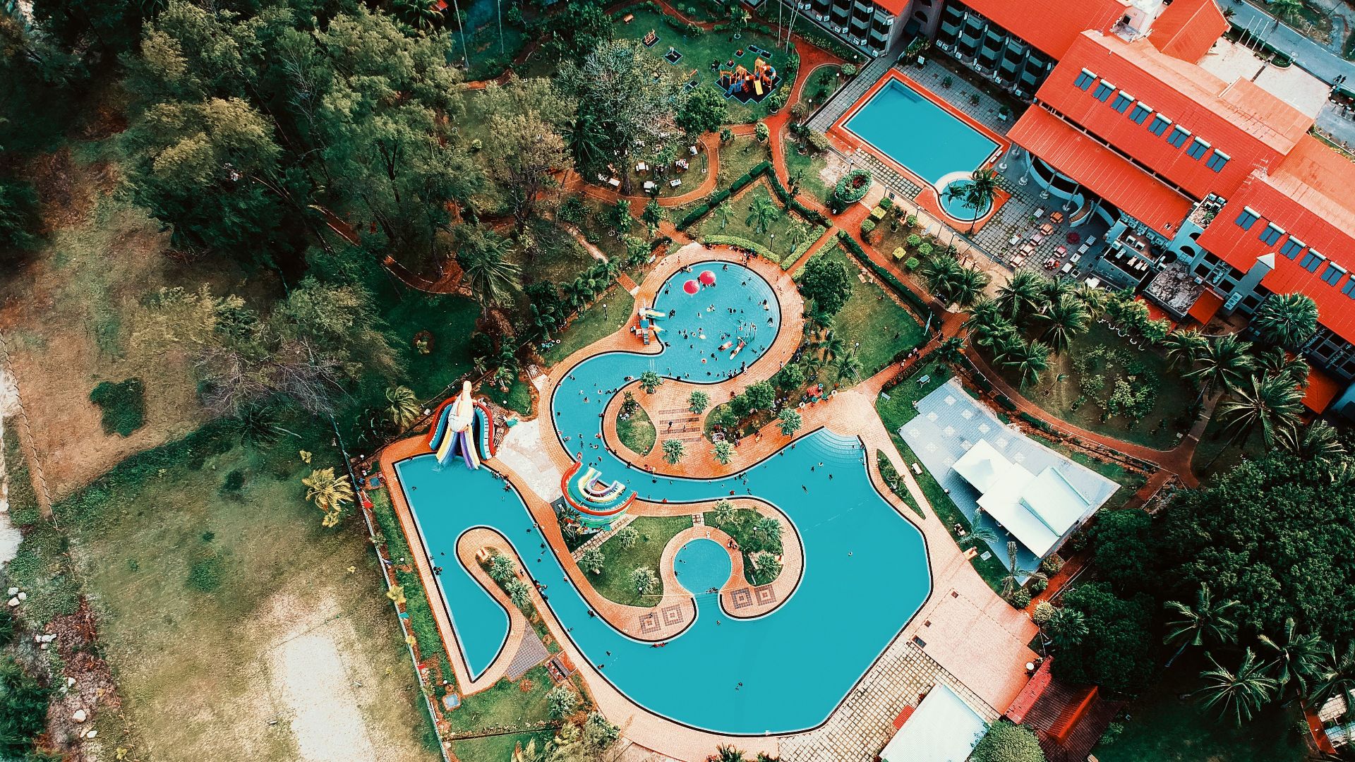 Colorful aerial shot of a resort featuring winding pools and lush gardens, perfect for summer vacations.