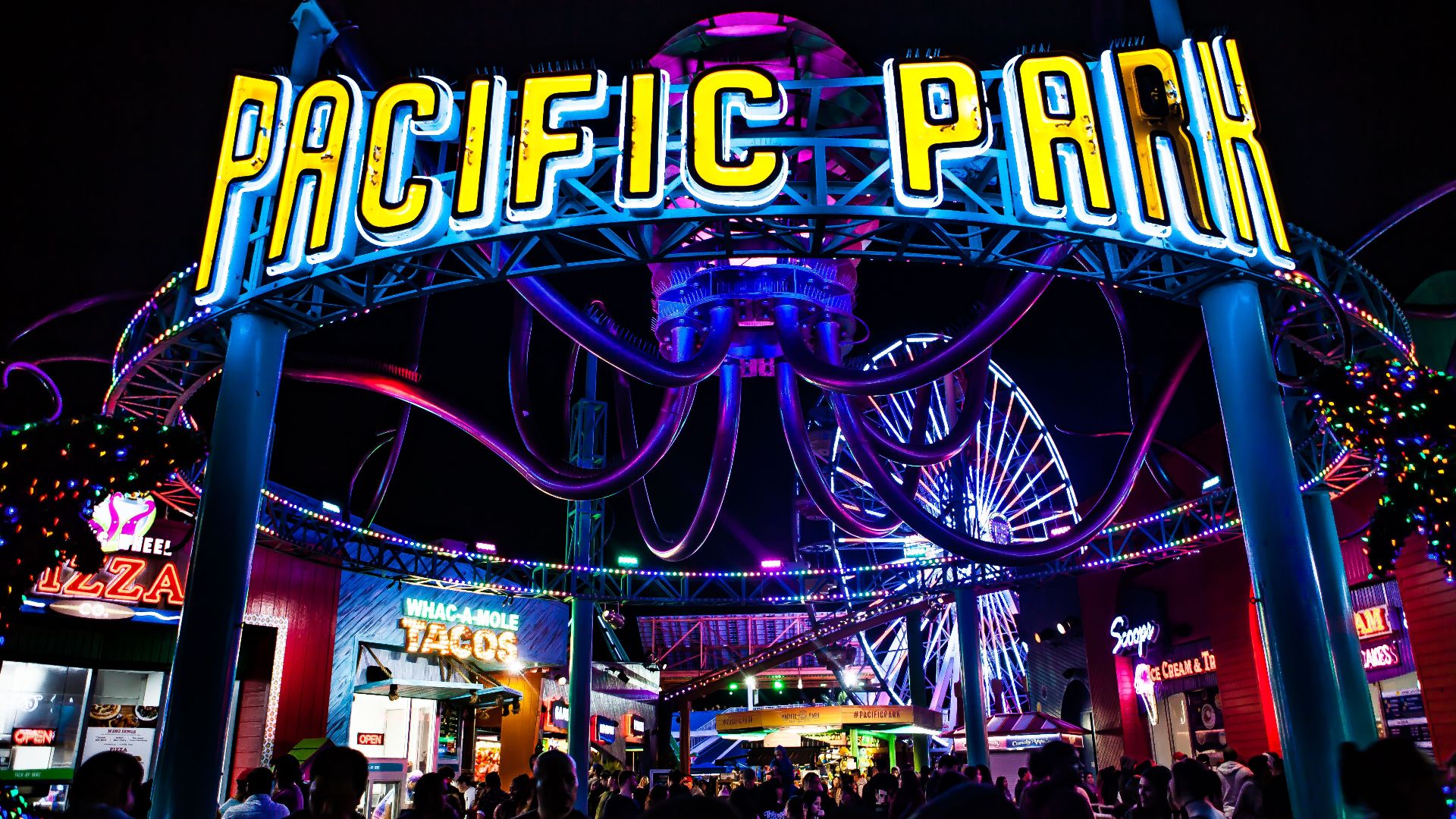 Colorful and lively night at Pacific Park with neon lights and a bustling crowd.