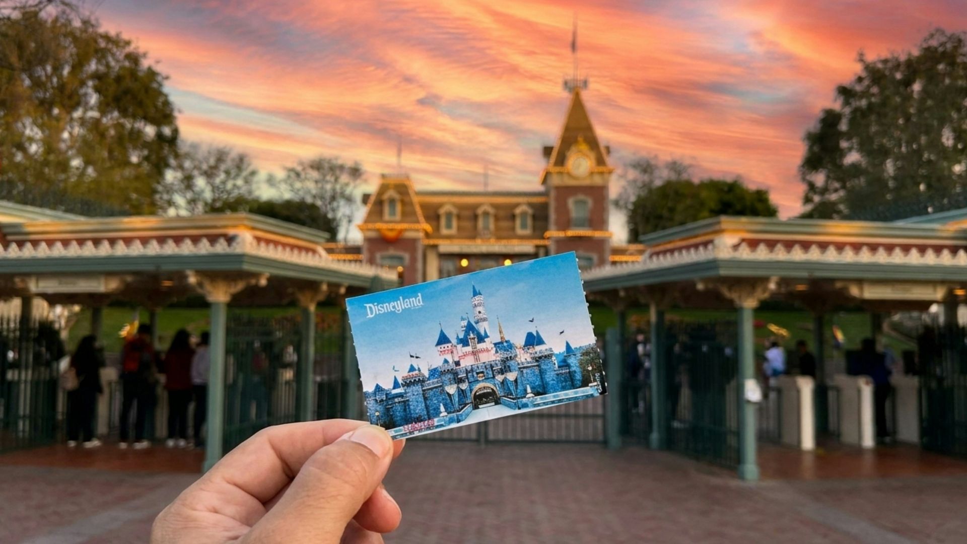 Hand holds disneyland ticket before park entrance at sunset.