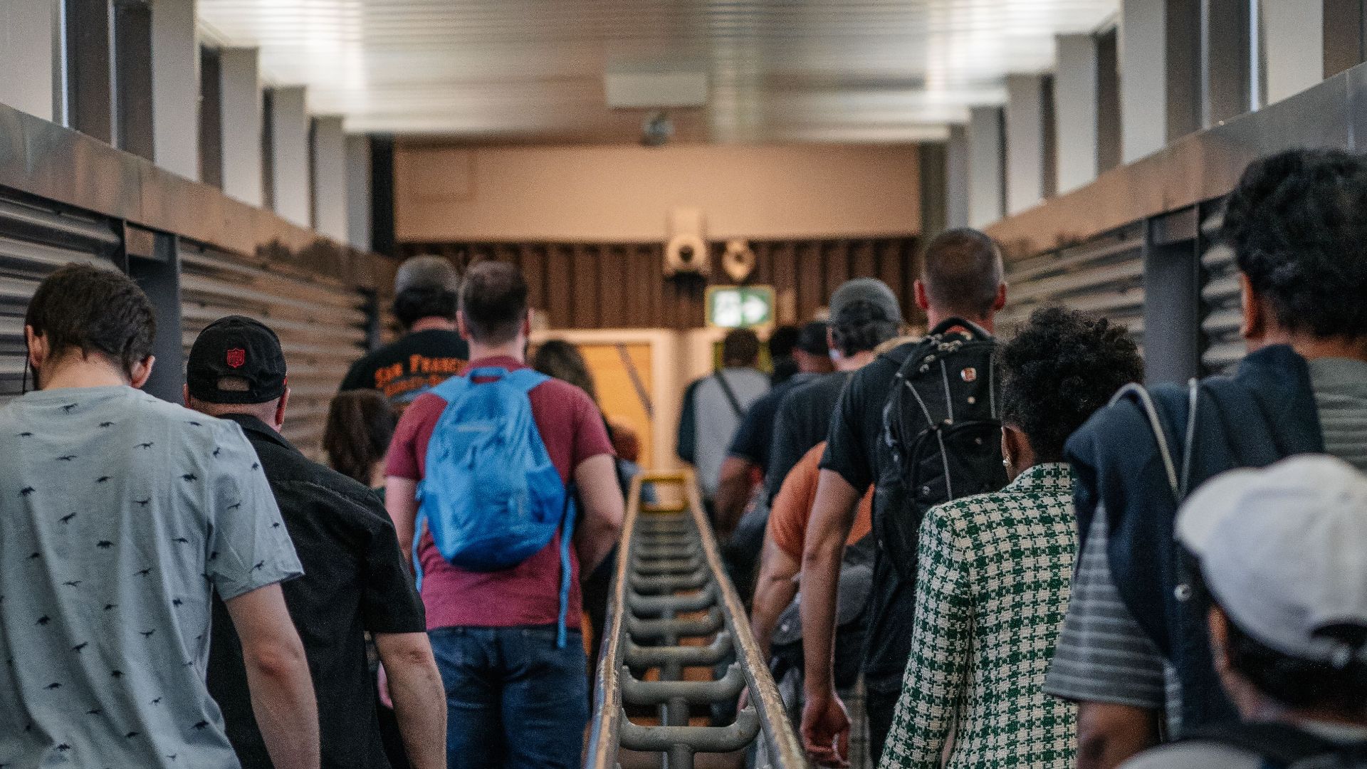 A group of diverse individuals walking along an indoor walkway with railings.