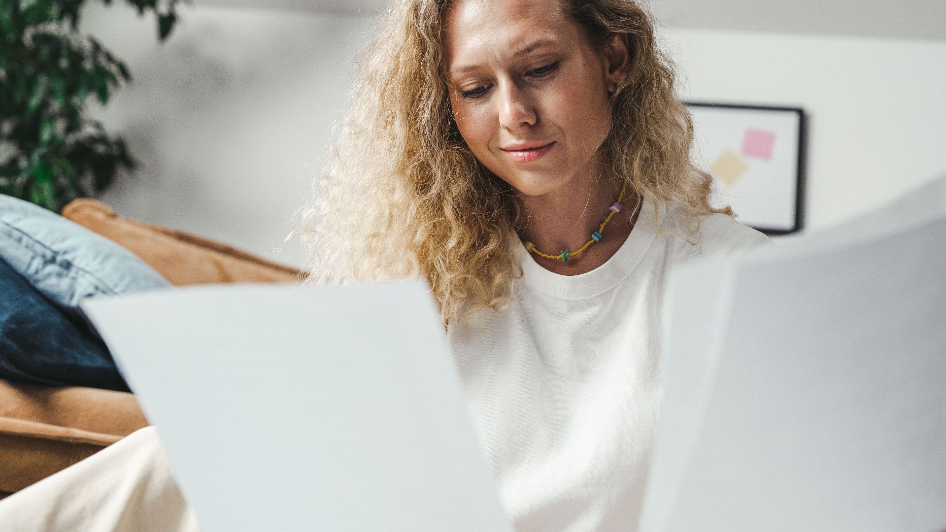 A woman with curly blonde hair analyzing papers while sitting indoors, conveying focus and determination.