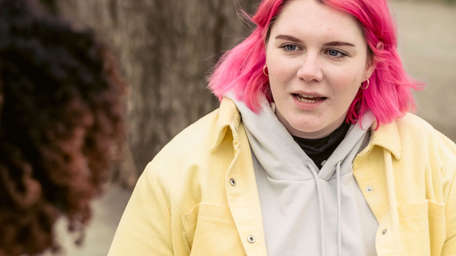 Woman with pink hair talking to crop anonymous man while sitting at wooden table with cans of soda on street
