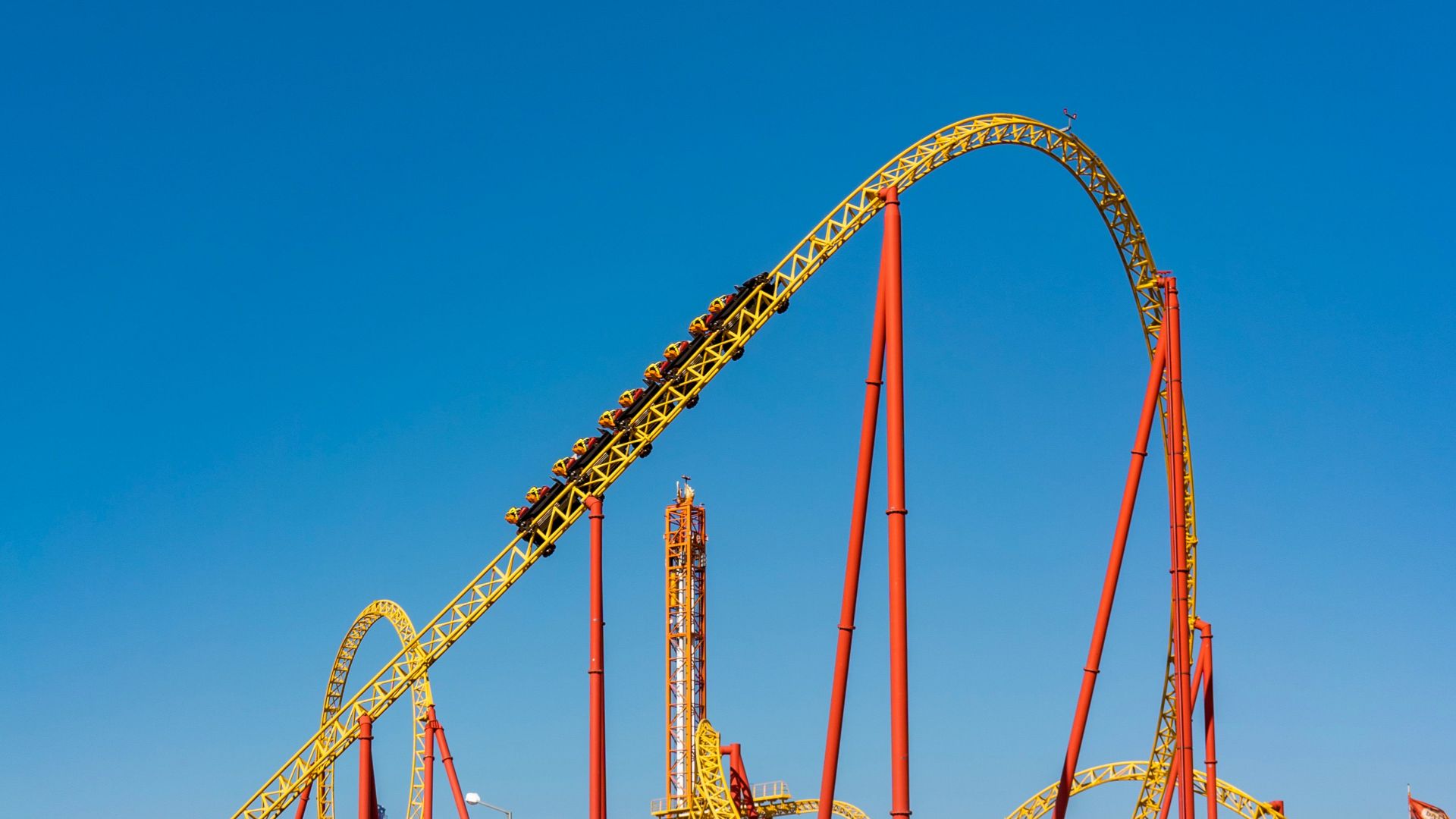 An exhilarating view of a roller coaster at an amusement park against a clear blue sky.