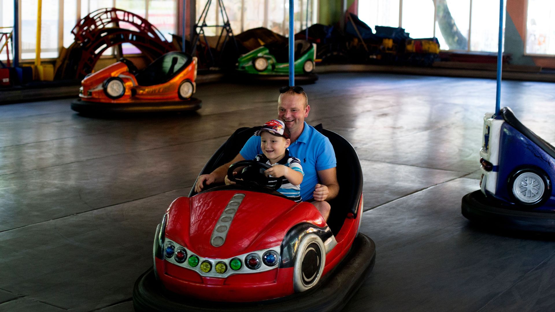 Playful moment of father and son driving a bumper car together indoors.