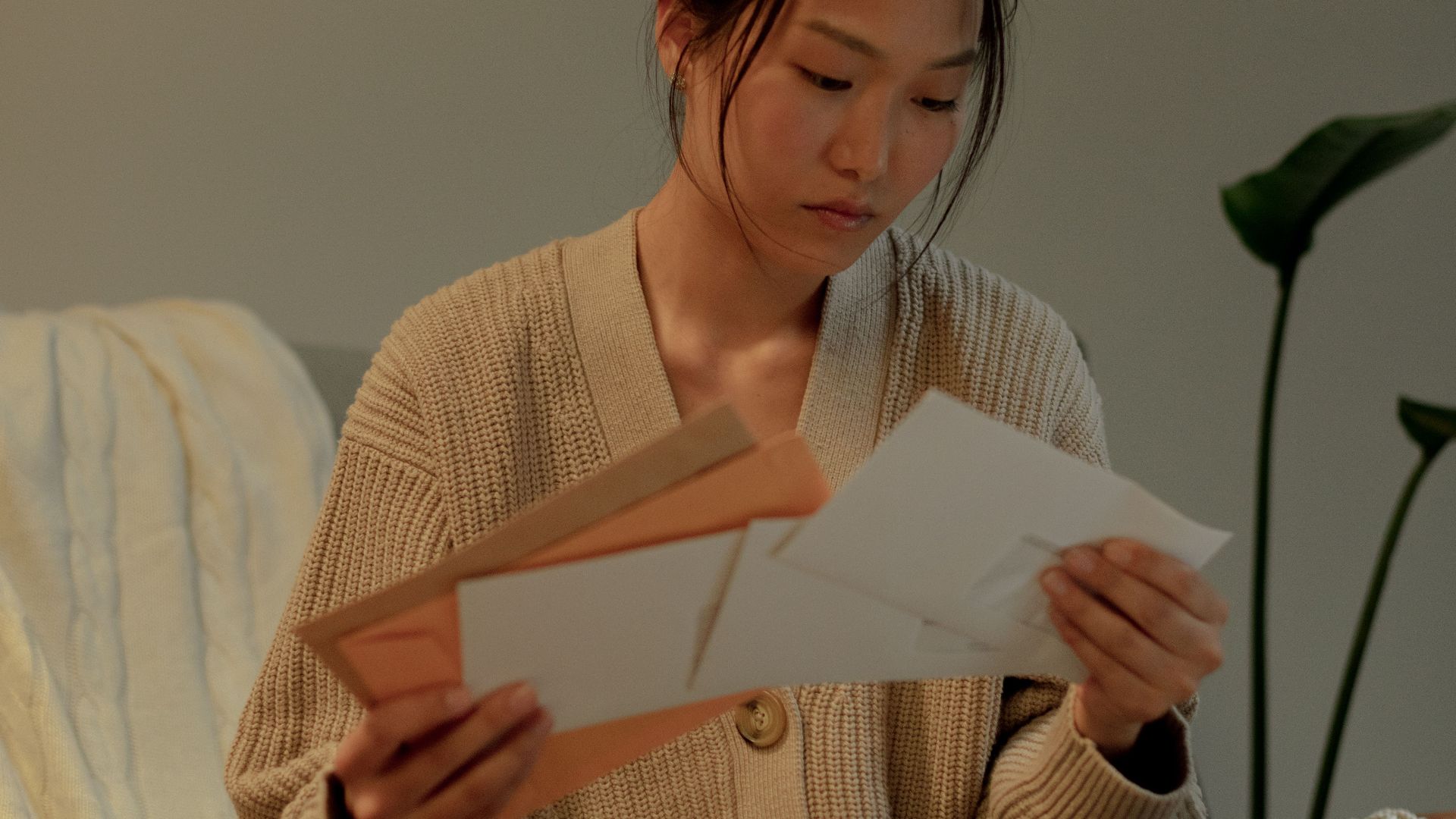 A woman seated in an armchair reads letters with focus, creating a warm, introspective mood.