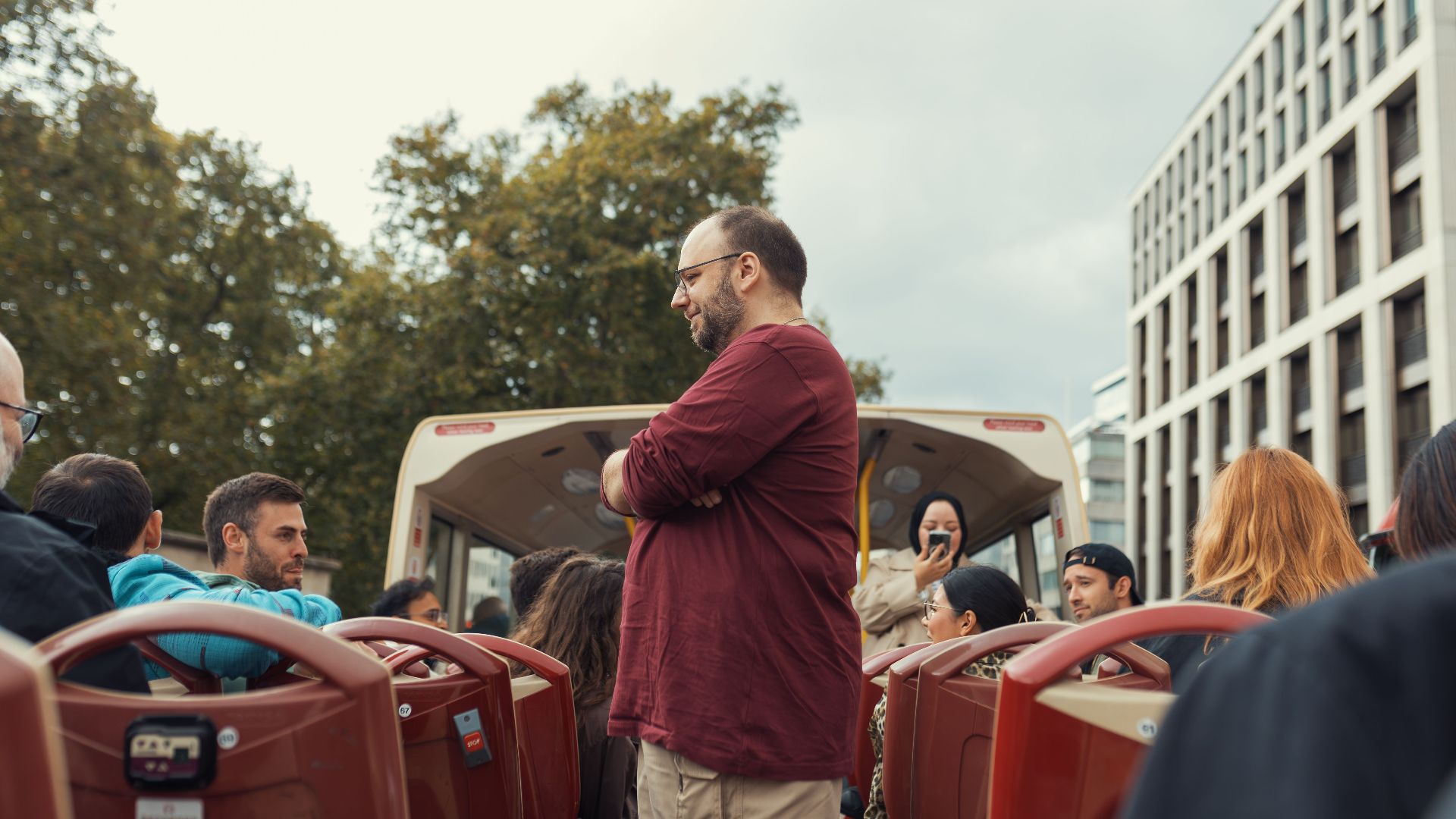 Group of people enjoying scenic open-top bus ride in an urban setting on a cloudy day.