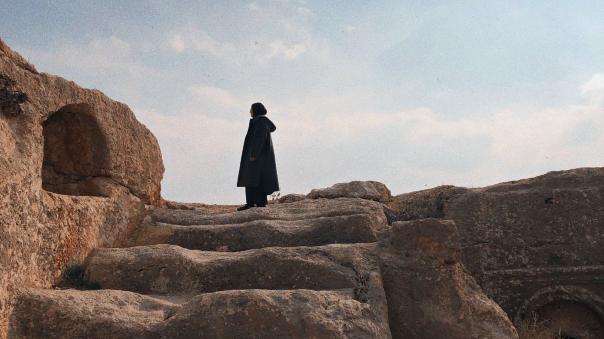 A solitary silhouette stands atop ancient stone steps under a vast, serene sky.