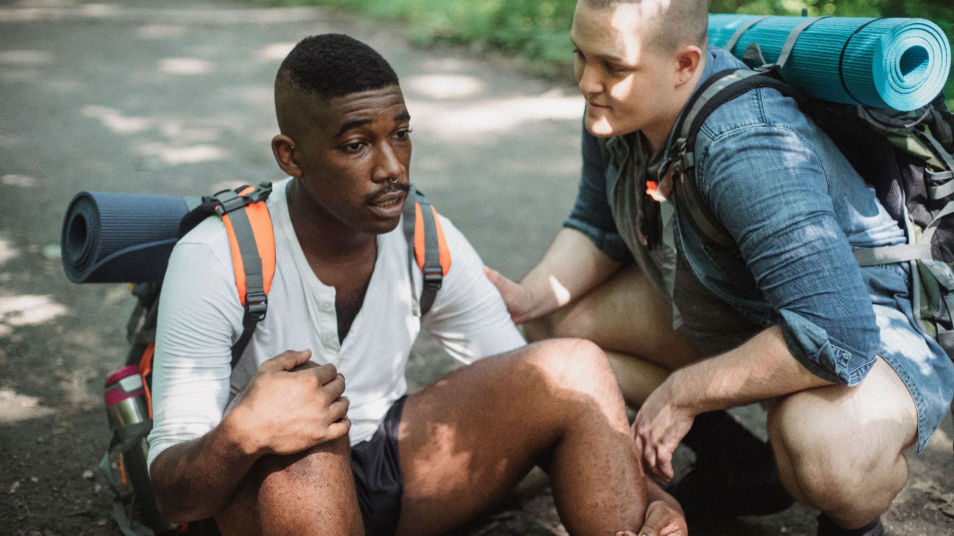 High angle of tired African American male tourist talking to friend while having break in difficult route in wildlife
