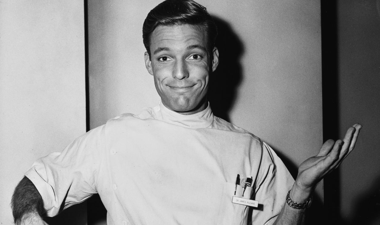 Getty Images - 1698604313 - American actor Richard Chamberlain in costume as his character 'Dr James Kildare' in the television drama 'Dr Kildare', holding a large pair of scissors in his right hand, his left raised with an open palm, at MGM Studios in Los Angeles, California.
