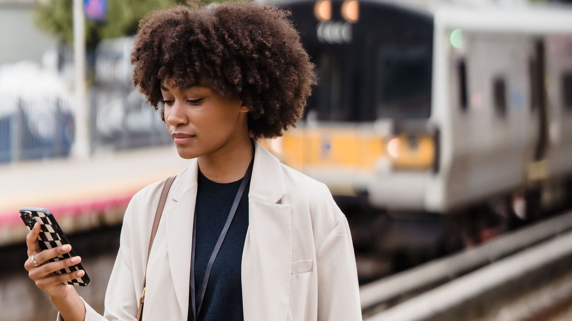 Young woman on train platform using smartphone, urban commute scene.