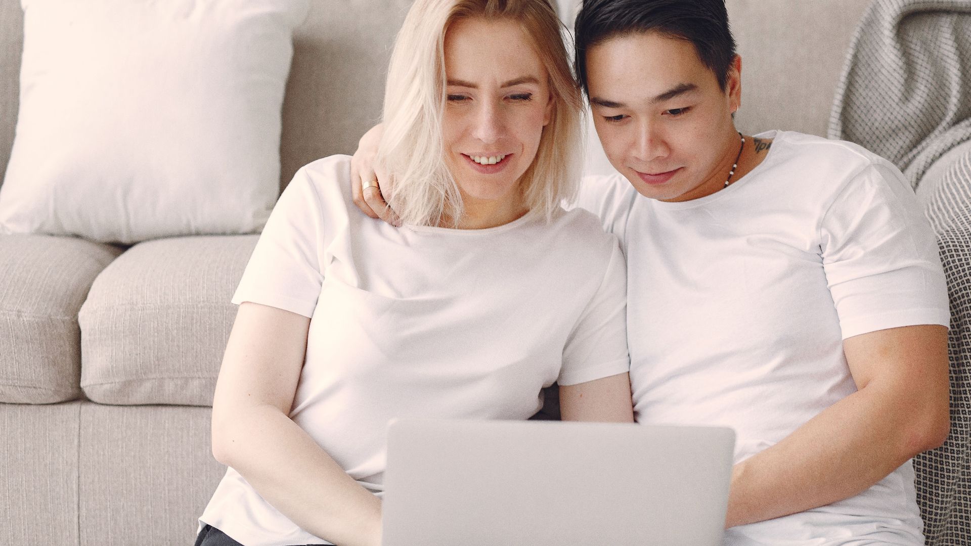 Smiling couple enjoying leisure time at home, watching something on a laptop while relaxing on the sofa.