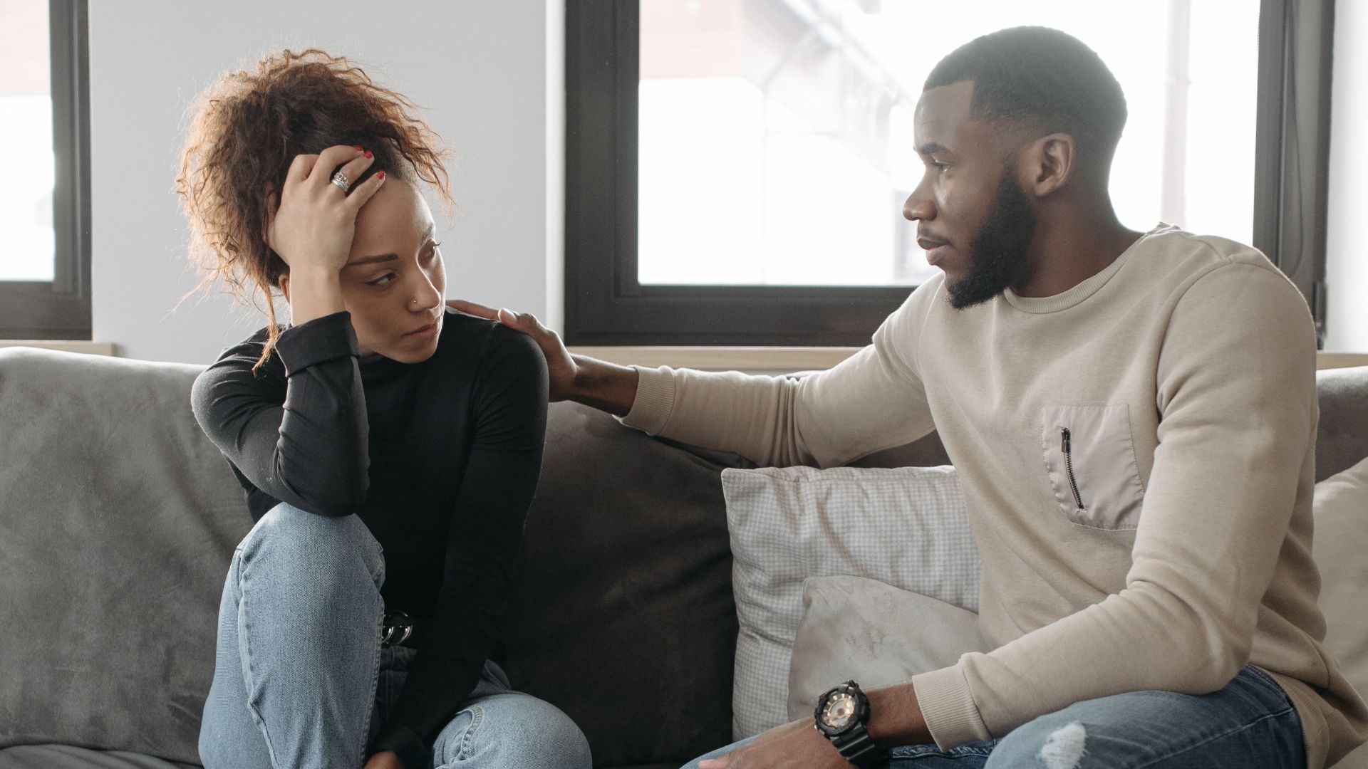 A couple shares a moment on their sofa at home, conveying care and understanding.