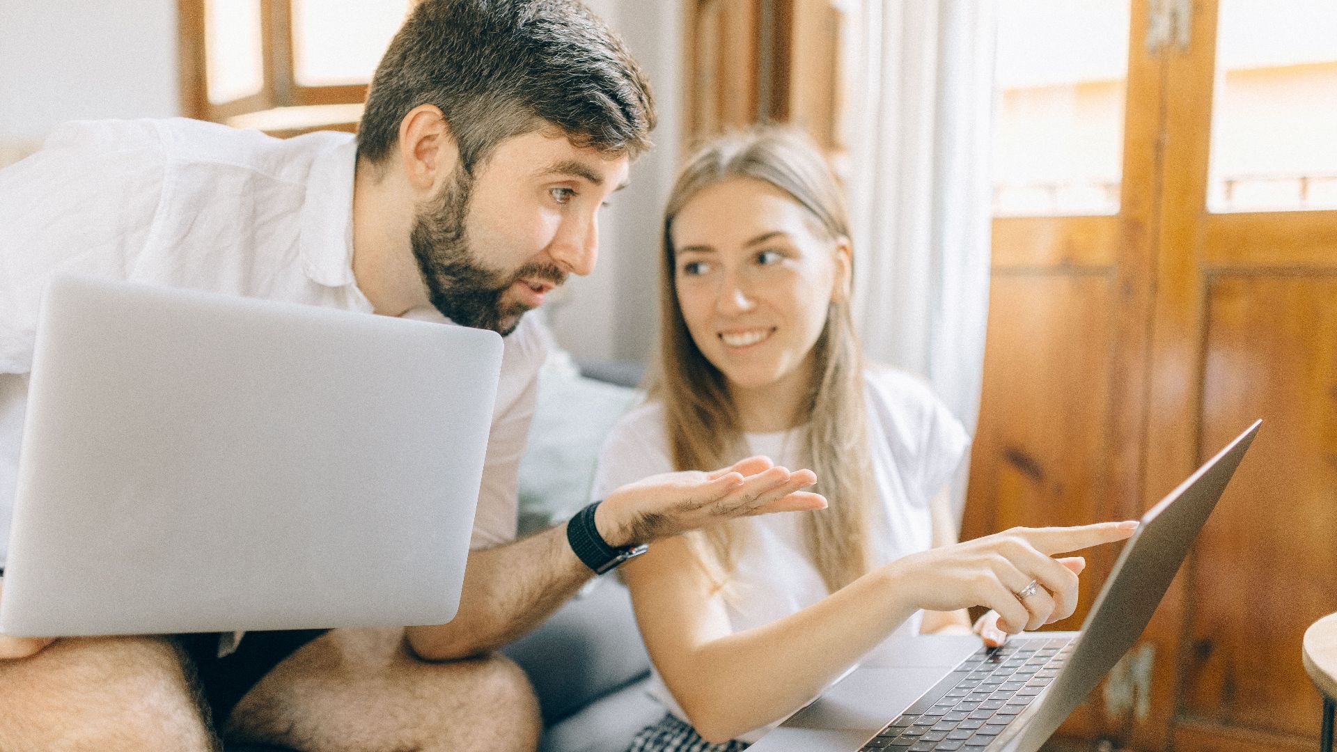 Young couple sitting together, discussing something on their laptops in a cozy room.