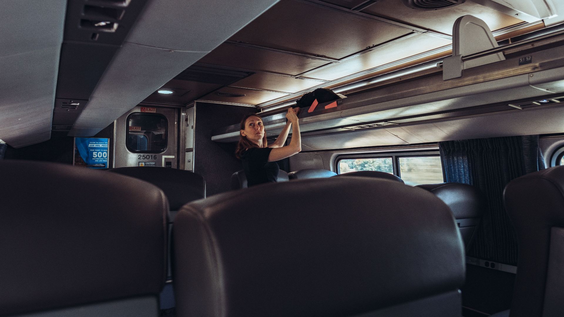 Female traveler stowing luggage in a train overhead compartment, emphasizing modern passenger travel.