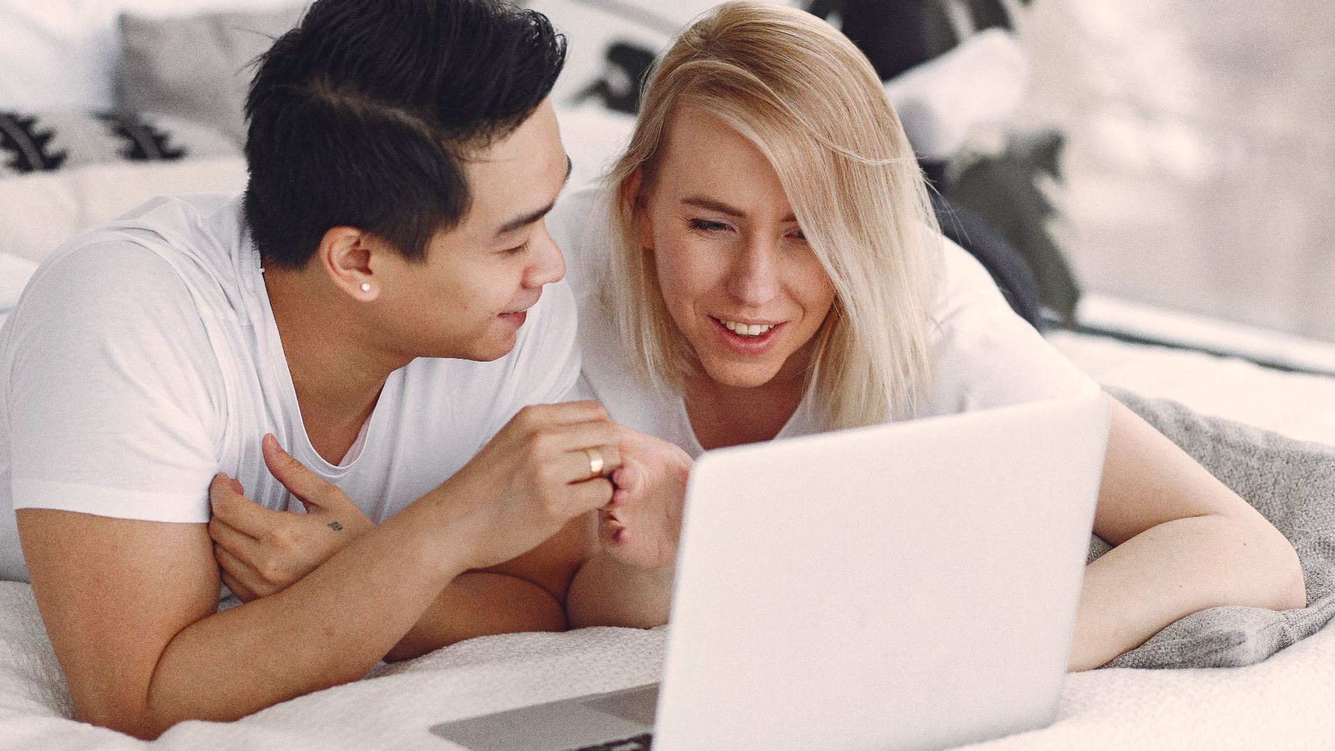 Happy couple enjoying leisure time indoors on laptop, sharing smiles and connection.
