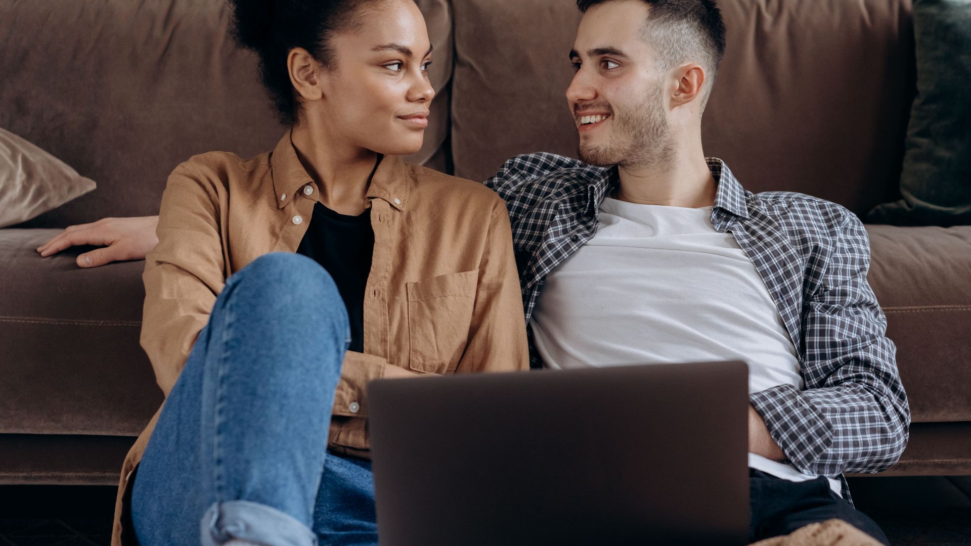 Happy couple sitting together on a couch with a laptop, enjoying each other's company.