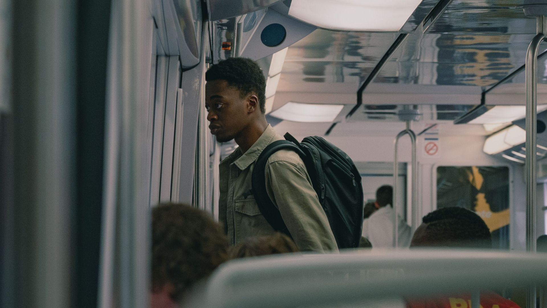 A young man standing inside a subway train, looking out the window during the day.