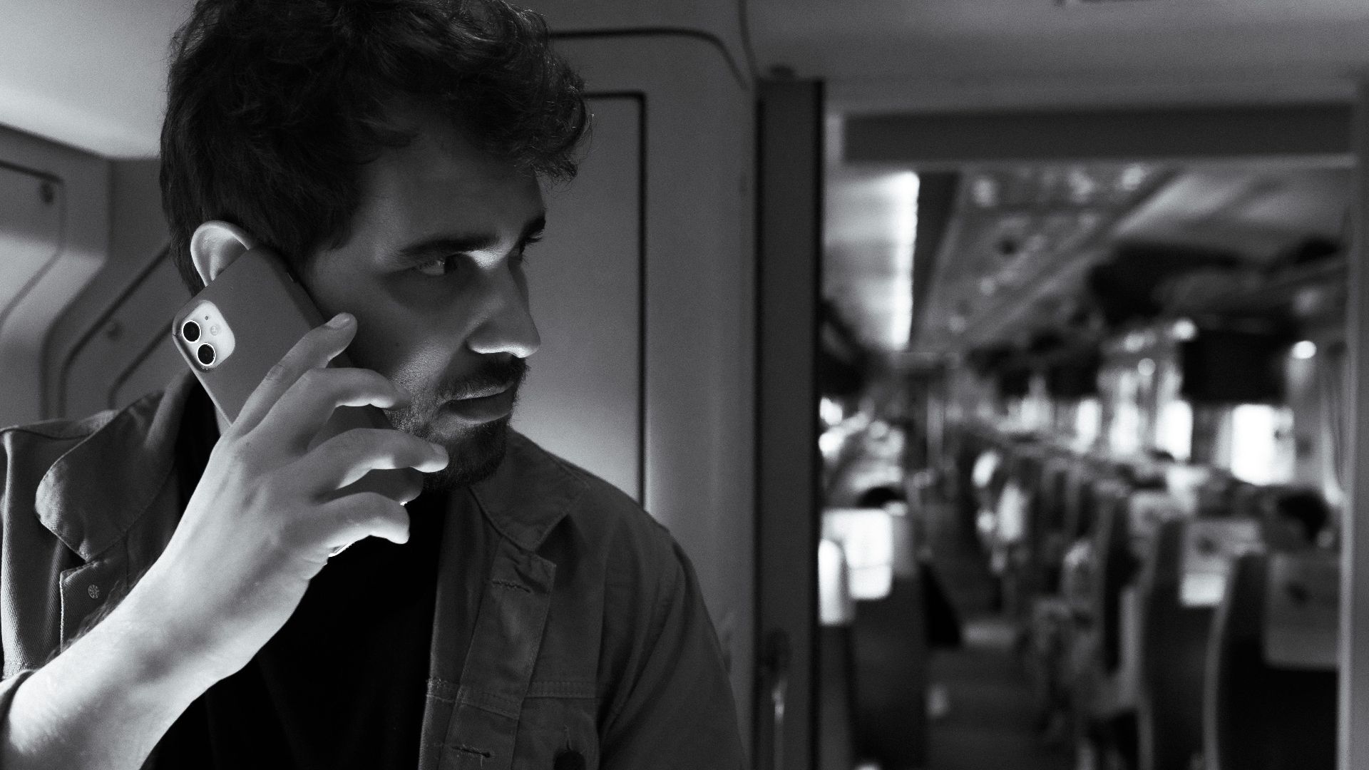 Black and white photo of a man using a smartphone while traveling on a modern train.