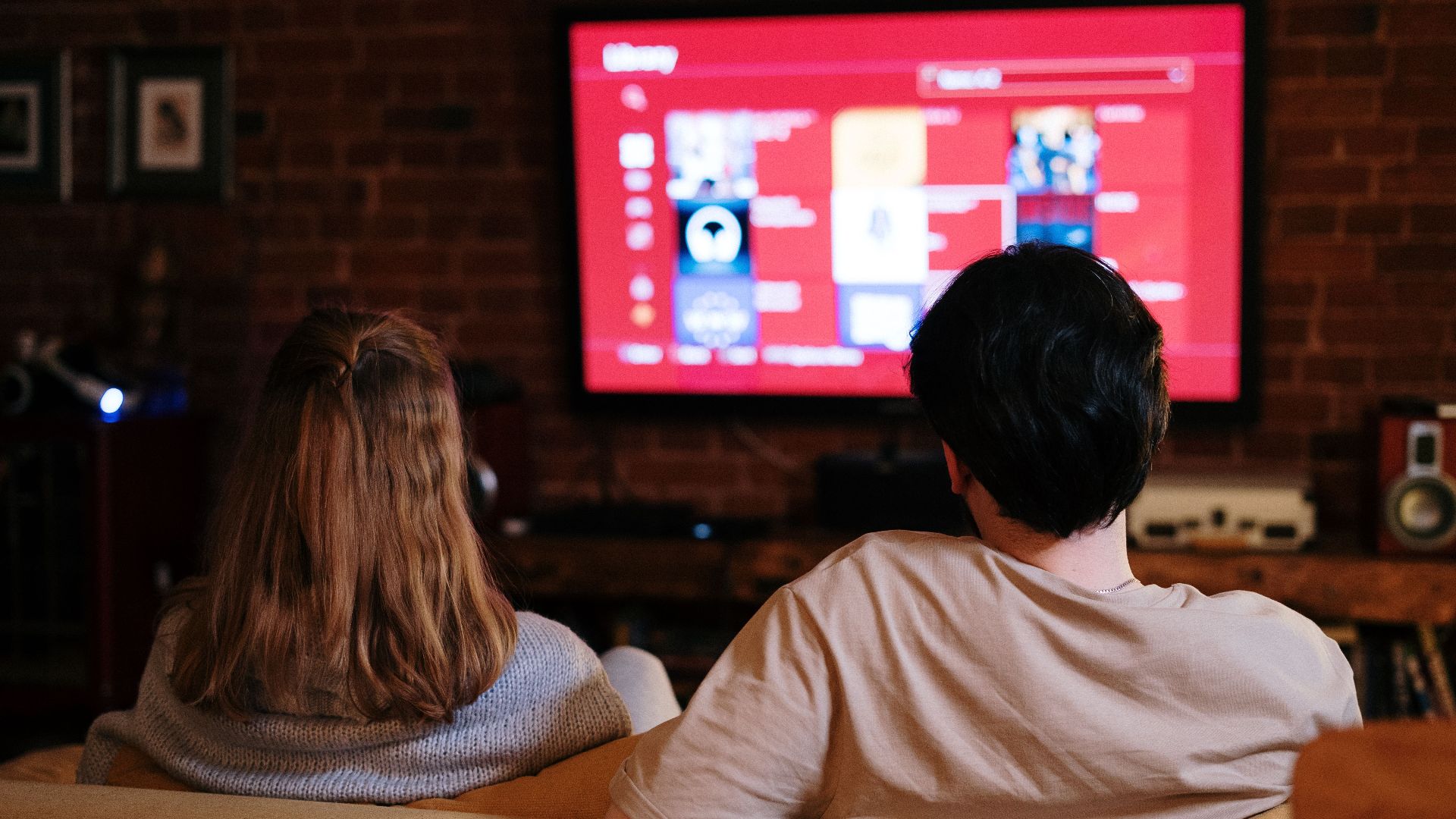 A couple enjoys streaming shows on a large TV in a cozy, brick-walled living room.